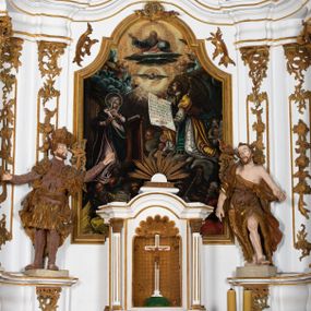 Zdjęcie nr 1: Kamienny ołtarz zamknięto w drewnianej obudowie, nakrywając go  drewnianą mensą z portatylem. Stipes ołtarzowy uzyskał kształt prostopadłościanu. Jego przód zdobi drewniane antepedium ujęte profilowaną ramą z malowanym chrystogramem "IHS" w glorii w polu. Na mensie ołtarza usytuowano tabernakulum w formie stojącego prostopadłościanu o wypukłym froncie i wklęsłych bokach wspierającego się na cokole. Jego przód ujmuje para kolumn podtrzymujących niepełne belkowanie, wyłamane nad ścianą frontową na kształt łuku odcinkowego nadwieszonego. Na froncie zamontowano obrotową, dwustronną niszę ujętą ramą w formie stojącego prostokąta zamkniętego łukiem półkolistym, wielolistnym. Nisze bębna zwieńczone zostały złoconymi konchami. Na tabernakulum usytuowano tron eucharystyczny w formie cokołu z leżącą księgą o siedmiu pieczęciach w glorii. Retabulum ołtarzowe wzniesiono na planie półowalu i polichromowano je na biało. Jest to architektoniczna, jednokondygnacyjna, jednoosiowa struktura ze zwieńczeniem. Po bokach flankują ją bramki ustawione na dwustrefowym, tralkowym, wklęsło-wypukłym cokole. Kondygnacja została ujęta dwiema parami pilastrów zwróconych delikatnie do wewnątrz oraz silnie wysuniętą do przodu parą kolumn o kapitelach kompozytowych. Podpory dźwigają pełne belkowanie o wklęsło-wypukłej linii. Nad polem środkowym belkowanie jest połączone gzymsem przyjmującym formę łuku falistego i wyłamane na osiach podpór. Kondygnacje ujmują spływy wolutowe połączone z łukowato wygiętymi wolutami podtrzymywanymi przez wysokie tralkowe cokoły, tworząc bramki ołtarza. W polu środkowym umieszczono obraz Zwiastowania ujęty profilowaną, złoconą ramą w formie stojącego prostokąta zamkniętego łukiem półkolistym nadwieszonym z uskokiem. Zwieńczenie uzyskało formę leżącego prostokąta flankowanego parą pilastrów zwróconych do wewnątrz oraz parą pilastrów zwróconych na zewnątrz, których trzony przechodzą w spływy wolutowe opadające na belkowanie. Pilastry dźwigają niepełne, wklęsło-wypukłe belkowanie przyjmujące nad polem formę łuku falistego. Całość wieńczy kartusz rokokowy z chrystogramem "IHS". W polu zwieńczenia znalazł się obraz św. Andrzeja w profilowanej, złoconej ramie o fantazyjnej formie zbliżonej do stojącego prostokąta. Pilastry kondygnacji ozdobiono kapitelami z rocaille'ów, a ich trzony udekorowano złoconymi, rokokowymi panneau ze zwisami utworzonymi z rocaille'ów, rozet i liści. Na ich tle usytuowano figury świętego króla i św. Jana Chrzciciela. Rzeźby stoją na górnej strefie cokołu na wspornikach z rocaille. Na ramie obrazu w polu środkowym, w przyłuczach i na belkowaniu znalazły się ornamenty roślinne. Z kolei na wolutowych łukach bramek umieszczono rokokowe wazony oraz pary figur aniołów z kartuszami. Na belkowaniu i wolutach zwieńczenia znajdują się dwie pary puttów. Także trzony pilastrów zwieńczenia dekorowane są złoconymi zwisami z rocaille'ów i kwiatów. Pole wokół obrazu św. Andrzeja zostało ozdobione fragmentami rocaille'ów. Pod gzymsem koronującym powyżej obrazu, podwieszono lambrekin, zdobiony przy górnej krawędzi złoconymi liśćmi i rocaille'm. 