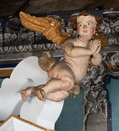 Zdjęcie nr 4: Kamienny ołtarz zamknięto w drewnianej obudowie, nakrywając go  drewnianą mensą z portatylem. Stipes ołtarzowy uzyskał kształt prostopadłościanu. Jego przód zdobi drewniane antepedium ujęte profilowaną ramą z malowanym chrystogramem "IHS" w glorii w polu. Na mensie ołtarza usytuowano tabernakulum w formie stojącego prostopadłościanu o wypukłym froncie i wklęsłych bokach wspierającego się na cokole. Jego przód ujmuje para kolumn podtrzymujących niepełne belkowanie, wyłamane nad ścianą frontową na kształt łuku odcinkowego nadwieszonego. Na froncie zamontowano obrotową, dwustronną niszę ujętą ramą w formie stojącego prostokąta zamkniętego łukiem półkolistym, wielolistnym. Nisze bębna zwieńczone zostały złoconymi konchami. Na tabernakulum usytuowano tron eucharystyczny w formie cokołu z leżącą księgą o siedmiu pieczęciach w glorii. Retabulum ołtarzowe wzniesiono na planie półowalu i polichromowano je na biało. Jest to architektoniczna, jednokondygnacyjna, jednoosiowa struktura ze zwieńczeniem. Po bokach flankują ją bramki ustawione na dwustrefowym, tralkowym, wklęsło-wypukłym cokole. Kondygnacja została ujęta dwiema parami pilastrów zwróconych delikatnie do wewnątrz oraz silnie wysuniętą do przodu parą kolumn o kapitelach kompozytowych. Podpory dźwigają pełne belkowanie o wklęsło-wypukłej linii. Nad polem środkowym belkowanie jest połączone gzymsem przyjmującym formę łuku falistego i wyłamane na osiach podpór. Kondygnacje ujmują spływy wolutowe połączone z łukowato wygiętymi wolutami podtrzymywanymi przez wysokie tralkowe cokoły, tworząc bramki ołtarza. W polu środkowym umieszczono obraz Zwiastowania ujęty profilowaną, złoconą ramą w formie stojącego prostokąta zamkniętego łukiem półkolistym nadwieszonym z uskokiem. Zwieńczenie uzyskało formę leżącego prostokąta flankowanego parą pilastrów zwróconych do wewnątrz oraz parą pilastrów zwróconych na zewnątrz, których trzony przechodzą w spływy wolutowe opadające na belkowanie. Pilastry dźwigają niepełne, wklęsło-wypukłe belkowanie przyjmujące nad polem formę łuku falistego. Całość wieńczy kartusz rokokowy z chrystogramem "IHS". W polu zwieńczenia znalazł się obraz św. Andrzeja w profilowanej, złoconej ramie o fantazyjnej formie zbliżonej do stojącego prostokąta. Pilastry kondygnacji ozdobiono kapitelami z rocaille'ów, a ich trzony udekorowano złoconymi, rokokowymi panneau ze zwisami utworzonymi z rocaille'ów, rozet i liści. Na ich tle usytuowano figury świętego króla i św. Jana Chrzciciela. Rzeźby stoją na górnej strefie cokołu na wspornikach z rocaille. Na ramie obrazu w polu środkowym, w przyłuczach i na belkowaniu znalazły się ornamenty roślinne. Z kolei na wolutowych łukach bramek umieszczono rokokowe wazony oraz pary figur aniołów z kartuszami. Na belkowaniu i wolutach zwieńczenia znajdują się dwie pary puttów. Także trzony pilastrów zwieńczenia dekorowane są złoconymi zwisami z rocaille'ów i kwiatów. Pole wokół obrazu św. Andrzeja zostało ozdobione fragmentami rocaille'ów. Pod gzymsem koronującym powyżej obrazu, podwieszono lambrekin, zdobiony przy górnej krawędzi złoconymi liśćmi i rocaille'm. 