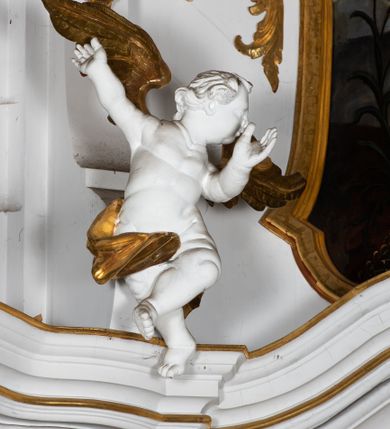 Zdjęcie nr 5: Kamienny ołtarz zamknięto w drewnianej obudowie, nakrywając go  drewnianą mensą z portatylem. Stipes ołtarzowy uzyskał kształt prostopadłościanu. Jego przód zdobi drewniane antepedium ujęte profilowaną ramą z malowanym chrystogramem "IHS" w glorii w polu. Na mensie ołtarza usytuowano tabernakulum w formie stojącego prostopadłościanu o wypukłym froncie i wklęsłych bokach wspierającego się na cokole. Jego przód ujmuje para kolumn podtrzymujących niepełne belkowanie, wyłamane nad ścianą frontową na kształt łuku odcinkowego nadwieszonego. Na froncie zamontowano obrotową, dwustronną niszę ujętą ramą w formie stojącego prostokąta zamkniętego łukiem półkolistym, wielolistnym. Nisze bębna zwieńczone zostały złoconymi konchami. Na tabernakulum usytuowano tron eucharystyczny w formie cokołu z leżącą księgą o siedmiu pieczęciach w glorii. Retabulum ołtarzowe wzniesiono na planie półowalu i polichromowano je na biało. Jest to architektoniczna, jednokondygnacyjna, jednoosiowa struktura ze zwieńczeniem. Po bokach flankują ją bramki ustawione na dwustrefowym, tralkowym, wklęsło-wypukłym cokole. Kondygnacja została ujęta dwiema parami pilastrów zwróconych delikatnie do wewnątrz oraz silnie wysuniętą do przodu parą kolumn o kapitelach kompozytowych. Podpory dźwigają pełne belkowanie o wklęsło-wypukłej linii. Nad polem środkowym belkowanie jest połączone gzymsem przyjmującym formę łuku falistego i wyłamane na osiach podpór. Kondygnacje ujmują spływy wolutowe połączone z łukowato wygiętymi wolutami podtrzymywanymi przez wysokie tralkowe cokoły, tworząc bramki ołtarza. W polu środkowym umieszczono obraz Zwiastowania ujęty profilowaną, złoconą ramą w formie stojącego prostokąta zamkniętego łukiem półkolistym nadwieszonym z uskokiem. Zwieńczenie uzyskało formę leżącego prostokąta flankowanego parą pilastrów zwróconych do wewnątrz oraz parą pilastrów zwróconych na zewnątrz, których trzony przechodzą w spływy wolutowe opadające na belkowanie. Pilastry dźwigają niepełne, wklęsło-wypukłe belkowanie przyjmujące nad polem formę łuku falistego. Całość wieńczy kartusz rokokowy z chrystogramem "IHS". W polu zwieńczenia znalazł się obraz św. Andrzeja w profilowanej, złoconej ramie o fantazyjnej formie zbliżonej do stojącego prostokąta. Pilastry kondygnacji ozdobiono kapitelami z rocaille'ów, a ich trzony udekorowano złoconymi, rokokowymi panneau ze zwisami utworzonymi z rocaille'ów, rozet i liści. Na ich tle usytuowano figury świętego króla i św. Jana Chrzciciela. Rzeźby stoją na górnej strefie cokołu na wspornikach z rocaille. Na ramie obrazu w polu środkowym, w przyłuczach i na belkowaniu znalazły się ornamenty roślinne. Z kolei na wolutowych łukach bramek umieszczono rokokowe wazony oraz pary figur aniołów z kartuszami. Na belkowaniu i wolutach zwieńczenia znajdują się dwie pary puttów. Także trzony pilastrów zwieńczenia dekorowane są złoconymi zwisami z rocaille'ów i kwiatów. Pole wokół obrazu św. Andrzeja zostało ozdobione fragmentami rocaille'ów. Pod gzymsem koronującym powyżej obrazu, podwieszono lambrekin, zdobiony przy górnej krawędzi złoconymi liśćmi i rocaille'm. 