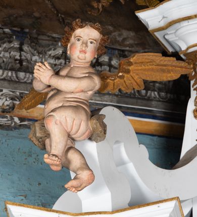 Zdjęcie nr 3: Kamienny ołtarz zamknięto w drewnianej obudowie, nakrywając go  drewnianą mensą z portatylem. Stipes ołtarzowy uzyskał kształt prostopadłościanu. Jego przód zdobi drewniane antepedium ujęte profilowaną ramą z malowanym chrystogramem "IHS" w glorii w polu. Na mensie ołtarza usytuowano tabernakulum w formie stojącego prostopadłościanu o wypukłym froncie i wklęsłych bokach wspierającego się na cokole. Jego przód ujmuje para kolumn podtrzymujących niepełne belkowanie, wyłamane nad ścianą frontową na kształt łuku odcinkowego nadwieszonego. Na froncie zamontowano obrotową, dwustronną niszę ujętą ramą w formie stojącego prostokąta zamkniętego łukiem półkolistym, wielolistnym. Nisze bębna zwieńczone zostały złoconymi konchami. Na tabernakulum usytuowano tron eucharystyczny w formie cokołu z leżącą księgą o siedmiu pieczęciach w glorii. Retabulum ołtarzowe wzniesiono na planie półowalu i polichromowano je na biało. Jest to architektoniczna, jednokondygnacyjna, jednoosiowa struktura ze zwieńczeniem. Po bokach flankują ją bramki ustawione na dwustrefowym, tralkowym, wklęsło-wypukłym cokole. Kondygnacja została ujęta dwiema parami pilastrów zwróconych delikatnie do wewnątrz oraz silnie wysuniętą do przodu parą kolumn o kapitelach kompozytowych. Podpory dźwigają pełne belkowanie o wklęsło-wypukłej linii. Nad polem środkowym belkowanie jest połączone gzymsem przyjmującym formę łuku falistego i wyłamane na osiach podpór. Kondygnacje ujmują spływy wolutowe połączone z łukowato wygiętymi wolutami podtrzymywanymi przez wysokie tralkowe cokoły, tworząc bramki ołtarza. W polu środkowym umieszczono obraz Zwiastowania ujęty profilowaną, złoconą ramą w formie stojącego prostokąta zamkniętego łukiem półkolistym nadwieszonym z uskokiem. Zwieńczenie uzyskało formę leżącego prostokąta flankowanego parą pilastrów zwróconych do wewnątrz oraz parą pilastrów zwróconych na zewnątrz, których trzony przechodzą w spływy wolutowe opadające na belkowanie. Pilastry dźwigają niepełne, wklęsło-wypukłe belkowanie przyjmujące nad polem formę łuku falistego. Całość wieńczy kartusz rokokowy z chrystogramem "IHS". W polu zwieńczenia znalazł się obraz św. Andrzeja w profilowanej, złoconej ramie o fantazyjnej formie zbliżonej do stojącego prostokąta. Pilastry kondygnacji ozdobiono kapitelami z rocaille'ów, a ich trzony udekorowano złoconymi, rokokowymi panneau ze zwisami utworzonymi z rocaille'ów, rozet i liści. Na ich tle usytuowano figury świętego króla i św. Jana Chrzciciela. Rzeźby stoją na górnej strefie cokołu na wspornikach z rocaille. Na ramie obrazu w polu środkowym, w przyłuczach i na belkowaniu znalazły się ornamenty roślinne. Z kolei na wolutowych łukach bramek umieszczono rokokowe wazony oraz pary figur aniołów z kartuszami. Na belkowaniu i wolutach zwieńczenia znajdują się dwie pary puttów. Także trzony pilastrów zwieńczenia dekorowane są złoconymi zwisami z rocaille'ów i kwiatów. Pole wokół obrazu św. Andrzeja zostało ozdobione fragmentami rocaille'ów. Pod gzymsem koronującym powyżej obrazu, podwieszono lambrekin, zdobiony przy górnej krawędzi złoconymi liśćmi i rocaille'm. 