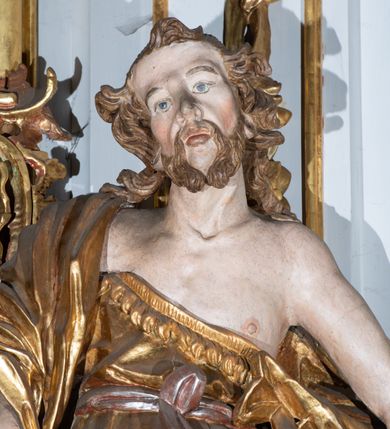 Zdjęcie nr 7: Kamienny ołtarz zamknięto w drewnianej obudowie, nakrywając go  drewnianą mensą z portatylem. Stipes ołtarzowy uzyskał kształt prostopadłościanu. Jego przód zdobi drewniane antepedium ujęte profilowaną ramą z malowanym chrystogramem "IHS" w glorii w polu. Na mensie ołtarza usytuowano tabernakulum w formie stojącego prostopadłościanu o wypukłym froncie i wklęsłych bokach wspierającego się na cokole. Jego przód ujmuje para kolumn podtrzymujących niepełne belkowanie, wyłamane nad ścianą frontową na kształt łuku odcinkowego nadwieszonego. Na froncie zamontowano obrotową, dwustronną niszę ujętą ramą w formie stojącego prostokąta zamkniętego łukiem półkolistym, wielolistnym. Nisze bębna zwieńczone zostały złoconymi konchami. Na tabernakulum usytuowano tron eucharystyczny w formie cokołu z leżącą księgą o siedmiu pieczęciach w glorii. Retabulum ołtarzowe wzniesiono na planie półowalu i polichromowano je na biało. Jest to architektoniczna, jednokondygnacyjna, jednoosiowa struktura ze zwieńczeniem. Po bokach flankują ją bramki ustawione na dwustrefowym, tralkowym, wklęsło-wypukłym cokole. Kondygnacja została ujęta dwiema parami pilastrów zwróconych delikatnie do wewnątrz oraz silnie wysuniętą do przodu parą kolumn o kapitelach kompozytowych. Podpory dźwigają pełne belkowanie o wklęsło-wypukłej linii. Nad polem środkowym belkowanie jest połączone gzymsem przyjmującym formę łuku falistego i wyłamane na osiach podpór. Kondygnacje ujmują spływy wolutowe połączone z łukowato wygiętymi wolutami podtrzymywanymi przez wysokie tralkowe cokoły, tworząc bramki ołtarza. W polu środkowym umieszczono obraz Zwiastowania ujęty profilowaną, złoconą ramą w formie stojącego prostokąta zamkniętego łukiem półkolistym nadwieszonym z uskokiem. Zwieńczenie uzyskało formę leżącego prostokąta flankowanego parą pilastrów zwróconych do wewnątrz oraz parą pilastrów zwróconych na zewnątrz, których trzony przechodzą w spływy wolutowe opadające na belkowanie. Pilastry dźwigają niepełne, wklęsło-wypukłe belkowanie przyjmujące nad polem formę łuku falistego. Całość wieńczy kartusz rokokowy z chrystogramem "IHS". W polu zwieńczenia znalazł się obraz św. Andrzeja w profilowanej, złoconej ramie o fantazyjnej formie zbliżonej do stojącego prostokąta. Pilastry kondygnacji ozdobiono kapitelami z rocaille'ów, a ich trzony udekorowano złoconymi, rokokowymi panneau ze zwisami utworzonymi z rocaille'ów, rozet i liści. Na ich tle usytuowano figury świętego króla i św. Jana Chrzciciela. Rzeźby stoją na górnej strefie cokołu na wspornikach z rocaille. Na ramie obrazu w polu środkowym, w przyłuczach i na belkowaniu znalazły się ornamenty roślinne. Z kolei na wolutowych łukach bramek umieszczono rokokowe wazony oraz pary figur aniołów z kartuszami. Na belkowaniu i wolutach zwieńczenia znajdują się dwie pary puttów. Także trzony pilastrów zwieńczenia dekorowane są złoconymi zwisami z rocaille'ów i kwiatów. Pole wokół obrazu św. Andrzeja zostało ozdobione fragmentami rocaille'ów. Pod gzymsem koronującym powyżej obrazu, podwieszono lambrekin, zdobiony przy górnej krawędzi złoconymi liśćmi i rocaille'm. 