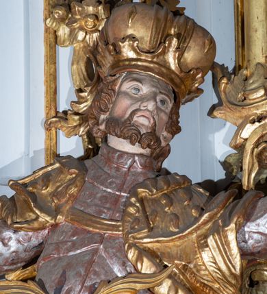 Zdjęcie nr 8: Kamienny ołtarz zamknięto w drewnianej obudowie, nakrywając go  drewnianą mensą z portatylem. Stipes ołtarzowy uzyskał kształt prostopadłościanu. Jego przód zdobi drewniane antepedium ujęte profilowaną ramą z malowanym chrystogramem "IHS" w glorii w polu. Na mensie ołtarza usytuowano tabernakulum w formie stojącego prostopadłościanu o wypukłym froncie i wklęsłych bokach wspierającego się na cokole. Jego przód ujmuje para kolumn podtrzymujących niepełne belkowanie, wyłamane nad ścianą frontową na kształt łuku odcinkowego nadwieszonego. Na froncie zamontowano obrotową, dwustronną niszę ujętą ramą w formie stojącego prostokąta zamkniętego łukiem półkolistym, wielolistnym. Nisze bębna zwieńczone zostały złoconymi konchami. Na tabernakulum usytuowano tron eucharystyczny w formie cokołu z leżącą księgą o siedmiu pieczęciach w glorii. Retabulum ołtarzowe wzniesiono na planie półowalu i polichromowano je na biało. Jest to architektoniczna, jednokondygnacyjna, jednoosiowa struktura ze zwieńczeniem. Po bokach flankują ją bramki ustawione na dwustrefowym, tralkowym, wklęsło-wypukłym cokole. Kondygnacja została ujęta dwiema parami pilastrów zwróconych delikatnie do wewnątrz oraz silnie wysuniętą do przodu parą kolumn o kapitelach kompozytowych. Podpory dźwigają pełne belkowanie o wklęsło-wypukłej linii. Nad polem środkowym belkowanie jest połączone gzymsem przyjmującym formę łuku falistego i wyłamane na osiach podpór. Kondygnacje ujmują spływy wolutowe połączone z łukowato wygiętymi wolutami podtrzymywanymi przez wysokie tralkowe cokoły, tworząc bramki ołtarza. W polu środkowym umieszczono obraz Zwiastowania ujęty profilowaną, złoconą ramą w formie stojącego prostokąta zamkniętego łukiem półkolistym nadwieszonym z uskokiem. Zwieńczenie uzyskało formę leżącego prostokąta flankowanego parą pilastrów zwróconych do wewnątrz oraz parą pilastrów zwróconych na zewnątrz, których trzony przechodzą w spływy wolutowe opadające na belkowanie. Pilastry dźwigają niepełne, wklęsło-wypukłe belkowanie przyjmujące nad polem formę łuku falistego. Całość wieńczy kartusz rokokowy z chrystogramem "IHS". W polu zwieńczenia znalazł się obraz św. Andrzeja w profilowanej, złoconej ramie o fantazyjnej formie zbliżonej do stojącego prostokąta. Pilastry kondygnacji ozdobiono kapitelami z rocaille'ów, a ich trzony udekorowano złoconymi, rokokowymi panneau ze zwisami utworzonymi z rocaille'ów, rozet i liści. Na ich tle usytuowano figury świętego króla i św. Jana Chrzciciela. Rzeźby stoją na górnej strefie cokołu na wspornikach z rocaille. Na ramie obrazu w polu środkowym, w przyłuczach i na belkowaniu znalazły się ornamenty roślinne. Z kolei na wolutowych łukach bramek umieszczono rokokowe wazony oraz pary figur aniołów z kartuszami. Na belkowaniu i wolutach zwieńczenia znajdują się dwie pary puttów. Także trzony pilastrów zwieńczenia dekorowane są złoconymi zwisami z rocaille'ów i kwiatów. Pole wokół obrazu św. Andrzeja zostało ozdobione fragmentami rocaille'ów. Pod gzymsem koronującym powyżej obrazu, podwieszono lambrekin, zdobiony przy górnej krawędzi złoconymi liśćmi i rocaille'm. 