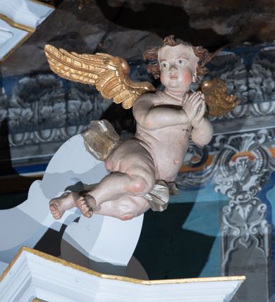 Zdjęcie nr 9: Kamienny ołtarz zamknięto w drewnianej obudowie, nakrywając go  drewnianą mensą z portatylem. Stipes ołtarzowy uzyskał kształt prostopadłościanu. Jego przód zdobi drewniane antepedium ujęte profilowaną ramą z malowanym chrystogramem "IHS" w glorii w polu. Na mensie ołtarza usytuowano tabernakulum w formie stojącego prostopadłościanu o wypukłym froncie i wklęsłych bokach wspierającego się na cokole. Jego przód ujmuje para kolumn podtrzymujących niepełne belkowanie, wyłamane nad ścianą frontową na kształt łuku odcinkowego nadwieszonego. Na froncie zamontowano obrotową, dwustronną niszę ujętą ramą w formie stojącego prostokąta zamkniętego łukiem półkolistym, wielolistnym. Nisze bębna zwieńczone zostały złoconymi konchami. Na tabernakulum usytuowano tron eucharystyczny w formie cokołu z leżącą księgą o siedmiu pieczęciach w glorii. Retabulum ołtarzowe wzniesiono na planie półowalu i polichromowano je na biało. Jest to architektoniczna, jednokondygnacyjna, jednoosiowa struktura ze zwieńczeniem. Po bokach flankują ją bramki ustawione na dwustrefowym, tralkowym, wklęsło-wypukłym cokole. Kondygnacja została ujęta dwiema parami pilastrów zwróconych delikatnie do wewnątrz oraz silnie wysuniętą do przodu parą kolumn o kapitelach kompozytowych. Podpory dźwigają pełne belkowanie o wklęsło-wypukłej linii. Nad polem środkowym belkowanie jest połączone gzymsem przyjmującym formę łuku falistego i wyłamane na osiach podpór. Kondygnacje ujmują spływy wolutowe połączone z łukowato wygiętymi wolutami podtrzymywanymi przez wysokie tralkowe cokoły, tworząc bramki ołtarza. W polu środkowym umieszczono obraz Zwiastowania ujęty profilowaną, złoconą ramą w formie stojącego prostokąta zamkniętego łukiem półkolistym nadwieszonym z uskokiem. Zwieńczenie uzyskało formę leżącego prostokąta flankowanego parą pilastrów zwróconych do wewnątrz oraz parą pilastrów zwróconych na zewnątrz, których trzony przechodzą w spływy wolutowe opadające na belkowanie. Pilastry dźwigają niepełne, wklęsło-wypukłe belkowanie przyjmujące nad polem formę łuku falistego. Całość wieńczy kartusz rokokowy z chrystogramem "IHS". W polu zwieńczenia znalazł się obraz św. Andrzeja w profilowanej, złoconej ramie o fantazyjnej formie zbliżonej do stojącego prostokąta. Pilastry kondygnacji ozdobiono kapitelami z rocaille'ów, a ich trzony udekorowano złoconymi, rokokowymi panneau ze zwisami utworzonymi z rocaille'ów, rozet i liści. Na ich tle usytuowano figury świętego króla i św. Jana Chrzciciela. Rzeźby stoją na górnej strefie cokołu na wspornikach z rocaille. Na ramie obrazu w polu środkowym, w przyłuczach i na belkowaniu znalazły się ornamenty roślinne. Z kolei na wolutowych łukach bramek umieszczono rokokowe wazony oraz pary figur aniołów z kartuszami. Na belkowaniu i wolutach zwieńczenia znajdują się dwie pary puttów. Także trzony pilastrów zwieńczenia dekorowane są złoconymi zwisami z rocaille'ów i kwiatów. Pole wokół obrazu św. Andrzeja zostało ozdobione fragmentami rocaille'ów. Pod gzymsem koronującym powyżej obrazu, podwieszono lambrekin, zdobiony przy górnej krawędzi złoconymi liśćmi i rocaille'm. 