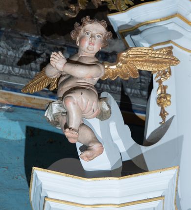 Zdjęcie nr 10: Kamienny ołtarz zamknięto w drewnianej obudowie, nakrywając go  drewnianą mensą z portatylem. Stipes ołtarzowy uzyskał kształt prostopadłościanu. Jego przód zdobi drewniane antepedium ujęte profilowaną ramą z malowanym chrystogramem "IHS" w glorii w polu. Na mensie ołtarza usytuowano tabernakulum w formie stojącego prostopadłościanu o wypukłym froncie i wklęsłych bokach wspierającego się na cokole. Jego przód ujmuje para kolumn podtrzymujących niepełne belkowanie, wyłamane nad ścianą frontową na kształt łuku odcinkowego nadwieszonego. Na froncie zamontowano obrotową, dwustronną niszę ujętą ramą w formie stojącego prostokąta zamkniętego łukiem półkolistym, wielolistnym. Nisze bębna zwieńczone zostały złoconymi konchami. Na tabernakulum usytuowano tron eucharystyczny w formie cokołu z leżącą księgą o siedmiu pieczęciach w glorii. Retabulum ołtarzowe wzniesiono na planie półowalu i polichromowano je na biało. Jest to architektoniczna, jednokondygnacyjna, jednoosiowa struktura ze zwieńczeniem. Po bokach flankują ją bramki ustawione na dwustrefowym, tralkowym, wklęsło-wypukłym cokole. Kondygnacja została ujęta dwiema parami pilastrów zwróconych delikatnie do wewnątrz oraz silnie wysuniętą do przodu parą kolumn o kapitelach kompozytowych. Podpory dźwigają pełne belkowanie o wklęsło-wypukłej linii. Nad polem środkowym belkowanie jest połączone gzymsem przyjmującym formę łuku falistego i wyłamane na osiach podpór. Kondygnacje ujmują spływy wolutowe połączone z łukowato wygiętymi wolutami podtrzymywanymi przez wysokie tralkowe cokoły, tworząc bramki ołtarza. W polu środkowym umieszczono obraz Zwiastowania ujęty profilowaną, złoconą ramą w formie stojącego prostokąta zamkniętego łukiem półkolistym nadwieszonym z uskokiem. Zwieńczenie uzyskało formę leżącego prostokąta flankowanego parą pilastrów zwróconych do wewnątrz oraz parą pilastrów zwróconych na zewnątrz, których trzony przechodzą w spływy wolutowe opadające na belkowanie. Pilastry dźwigają niepełne, wklęsło-wypukłe belkowanie przyjmujące nad polem formę łuku falistego. Całość wieńczy kartusz rokokowy z chrystogramem "IHS". W polu zwieńczenia znalazł się obraz św. Andrzeja w profilowanej, złoconej ramie o fantazyjnej formie zbliżonej do stojącego prostokąta. Pilastry kondygnacji ozdobiono kapitelami z rocaille'ów, a ich trzony udekorowano złoconymi, rokokowymi panneau ze zwisami utworzonymi z rocaille'ów, rozet i liści. Na ich tle usytuowano figury świętego króla i św. Jana Chrzciciela. Rzeźby stoją na górnej strefie cokołu na wspornikach z rocaille. Na ramie obrazu w polu środkowym, w przyłuczach i na belkowaniu znalazły się ornamenty roślinne. Z kolei na wolutowych łukach bramek umieszczono rokokowe wazony oraz pary figur aniołów z kartuszami. Na belkowaniu i wolutach zwieńczenia znajdują się dwie pary puttów. Także trzony pilastrów zwieńczenia dekorowane są złoconymi zwisami z rocaille'ów i kwiatów. Pole wokół obrazu św. Andrzeja zostało ozdobione fragmentami rocaille'ów. Pod gzymsem koronującym powyżej obrazu, podwieszono lambrekin, zdobiony przy górnej krawędzi złoconymi liśćmi i rocaille'm. 