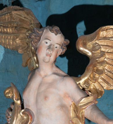 Zdjęcie nr 14: Kamienny ołtarz zamknięto w drewnianej obudowie, nakrywając go  drewnianą mensą z portatylem. Stipes ołtarzowy uzyskał kształt prostopadłościanu. Jego przód zdobi drewniane antepedium ujęte profilowaną ramą z malowanym chrystogramem &quot;IHS&quot; w glorii w polu. Na mensie ołtarza usytuowano tabernakulum w formie stojącego prostopadłościanu o wypukłym froncie i wklęsłych bokach wspierającego się na cokole. Jego przód ujmuje para kolumn podtrzymujących niepełne belkowanie, wyłamane nad ścianą frontową na kształt łuku odcinkowego nadwieszonego. Na froncie zamontowano obrotową, dwustronną niszę ujętą ramą w formie stojącego prostokąta zamkniętego łukiem półkolistym, wielolistnym. Nisze bębna zwieńczone zostały złoconymi konchami. Na tabernakulum usytuowano tron eucharystyczny w formie cokołu z leżącą księgą o siedmiu pieczęciach w glorii. Retabulum ołtarzowe wzniesiono na planie półowalu i polichromowano je na biało. Jest to architektoniczna, jednokondygnacyjna, jednoosiowa struktura ze zwieńczeniem. Po bokach flankują ją bramki ustawione na dwustrefowym, tralkowym, wklęsło-wypukłym cokole. Kondygnacja została ujęta dwiema parami pilastrów zwróconych delikatnie do wewnątrz oraz silnie wysuniętą do przodu parą kolumn o kapitelach kompozytowych. Podpory dźwigają pełne belkowanie o wklęsło-wypukłej linii. Nad polem środkowym belkowanie jest połączone gzymsem przyjmującym formę łuku falistego i wyłamane na osiach podpór. Kondygnacje ujmują spływy wolutowe połączone z łukowato wygiętymi wolutami podtrzymywanymi przez wysokie tralkowe cokoły, tworząc bramki ołtarza. W polu środkowym umieszczono obraz Zwiastowania ujęty profilowaną, złoconą ramą w formie stojącego prostokąta zamkniętego łukiem półkolistym nadwieszonym z uskokiem. Zwieńczenie uzyskało formę leżącego prostokąta flankowanego parą pilastrów zwróconych do wewnątrz oraz parą pilastrów zwróconych na zewnątrz, których trzony przechodzą w spływy wolutowe opadające na belkowanie. Pilastry dźwigają niepełne, wklęsło-wypukłe belkowanie przyjmujące nad polem formę łuku falistego. Całość wieńczy kartusz rokokowy z chrystogramem &quot;IHS&quot;. W polu zwieńczenia znalazł się obraz św. Andrzeja w profilowanej, złoconej ramie o fantazyjnej formie zbliżonej do stojącego prostokąta. Pilastry kondygnacji ozdobiono kapitelami z rocaille&#039;ów, a ich trzony udekorowano złoconymi, rokokowymi panneau ze zwisami utworzonymi z rocaille&#039;ów, rozet i liści. Na ich tle usytuowano figury świętego króla i św. Jana Chrzciciela. Rzeźby stoją na górnej strefie cokołu na wspornikach z rocaille. Na ramie obrazu w polu środkowym, w przyłuczach i na belkowaniu znalazły się ornamenty roślinne. Z kolei na wolutowych łukach bramek umieszczono rokokowe wazony oraz pary figur aniołów z kartuszami. Na belkowaniu i wolutach zwieńczenia znajdują się dwie pary puttów. Także trzony pilastrów zwieńczenia dekorowane są złoconymi zwisami z rocaille&#039;ów i kwiatów. Pole wokół obrazu św. Andrzeja zostało ozdobione fragmentami rocaille&#039;ów. Pod gzymsem koronującym powyżej obrazu, podwieszono lambrekin, zdobiony przy górnej krawędzi złoconymi liśćmi i rocaille&#039;m. 