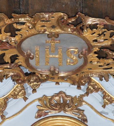 Zdjęcie nr 12: Kamienny ołtarz zamknięto w drewnianej obudowie, nakrywając go  drewnianą mensą z portatylem. Stipes ołtarzowy uzyskał kształt prostopadłościanu. Jego przód zdobi drewniane antepedium ujęte profilowaną ramą z malowanym chrystogramem "IHS" w glorii w polu. Na mensie ołtarza usytuowano tabernakulum w formie stojącego prostopadłościanu o wypukłym froncie i wklęsłych bokach wspierającego się na cokole. Jego przód ujmuje para kolumn podtrzymujących niepełne belkowanie, wyłamane nad ścianą frontową na kształt łuku odcinkowego nadwieszonego. Na froncie zamontowano obrotową, dwustronną niszę ujętą ramą w formie stojącego prostokąta zamkniętego łukiem półkolistym, wielolistnym. Nisze bębna zwieńczone zostały złoconymi konchami. Na tabernakulum usytuowano tron eucharystyczny w formie cokołu z leżącą księgą o siedmiu pieczęciach w glorii. Retabulum ołtarzowe wzniesiono na planie półowalu i polichromowano je na biało. Jest to architektoniczna, jednokondygnacyjna, jednoosiowa struktura ze zwieńczeniem. Po bokach flankują ją bramki ustawione na dwustrefowym, tralkowym, wklęsło-wypukłym cokole. Kondygnacja została ujęta dwiema parami pilastrów zwróconych delikatnie do wewnątrz oraz silnie wysuniętą do przodu parą kolumn o kapitelach kompozytowych. Podpory dźwigają pełne belkowanie o wklęsło-wypukłej linii. Nad polem środkowym belkowanie jest połączone gzymsem przyjmującym formę łuku falistego i wyłamane na osiach podpór. Kondygnacje ujmują spływy wolutowe połączone z łukowato wygiętymi wolutami podtrzymywanymi przez wysokie tralkowe cokoły, tworząc bramki ołtarza. W polu środkowym umieszczono obraz Zwiastowania ujęty profilowaną, złoconą ramą w formie stojącego prostokąta zamkniętego łukiem półkolistym nadwieszonym z uskokiem. Zwieńczenie uzyskało formę leżącego prostokąta flankowanego parą pilastrów zwróconych do wewnątrz oraz parą pilastrów zwróconych na zewnątrz, których trzony przechodzą w spływy wolutowe opadające na belkowanie. Pilastry dźwigają niepełne, wklęsło-wypukłe belkowanie przyjmujące nad polem formę łuku falistego. Całość wieńczy kartusz rokokowy z chrystogramem "IHS". W polu zwieńczenia znalazł się obraz św. Andrzeja w profilowanej, złoconej ramie o fantazyjnej formie zbliżonej do stojącego prostokąta. Pilastry kondygnacji ozdobiono kapitelami z rocaille'ów, a ich trzony udekorowano złoconymi, rokokowymi panneau ze zwisami utworzonymi z rocaille'ów, rozet i liści. Na ich tle usytuowano figury świętego króla i św. Jana Chrzciciela. Rzeźby stoją na górnej strefie cokołu na wspornikach z rocaille. Na ramie obrazu w polu środkowym, w przyłuczach i na belkowaniu znalazły się ornamenty roślinne. Z kolei na wolutowych łukach bramek umieszczono rokokowe wazony oraz pary figur aniołów z kartuszami. Na belkowaniu i wolutach zwieńczenia znajdują się dwie pary puttów. Także trzony pilastrów zwieńczenia dekorowane są złoconymi zwisami z rocaille'ów i kwiatów. Pole wokół obrazu św. Andrzeja zostało ozdobione fragmentami rocaille'ów. Pod gzymsem koronującym powyżej obrazu, podwieszono lambrekin, zdobiony przy górnej krawędzi złoconymi liśćmi i rocaille'm. 