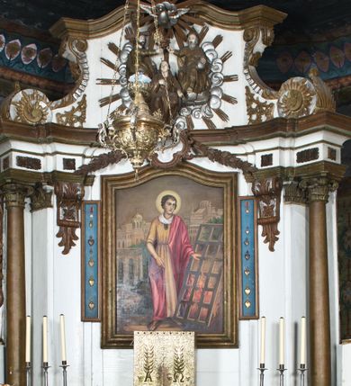 Zdjęcie nr 7: Nastawa ołtarzowa na planie półowalu uzyskała architektoniczną, jednokondygnacyjną strukturę ze zwieńczeniem. Jednoosiowe retabulum flankowane bramkami, na których ustawiono figury św. Wojciecha i św. Stanisława. Stipes ołtarz ujmuje drewniana prostopadłościenna obudowa podtrzymująca drewnianą mensą z portatylem. Drewniane antependium ujęte zostało czworoboczną, profilowaną ramą z płaskorzeźbionym i złoconym barankiem apokaliptycznym leżącym na księdze. Na mensie ustawiono współczesne tabernakulum pancerne w formie prostopadłościennej skrzynki. Kondygnacja retabulum ujęta została dwiema parami pilastrów zwróconych delikatnie do wewnątrz oraz silnie wysuniętą do przodu parą kolumn o kapitelach kompozytowych oraz dwie wolutowe konsole. Podpory dźwigają pełne belkowanie wsparte na impostach, o wklęsło-wypukłej linii. Nad polem środkowym widoczne jest połączenie wyłącznie gzymsem przyjmującym formę łuku falistego, wyłamane na osiach podpór. Na środku belkowania umieszczono kartusz, od którego odchodzą dwie girland kwiatowe. Kondygnacje ujmują zredukowane do wici akantowej uszaki. W polu środkowym usytuowano obraz św. Wawrzyńca ujęty profilowaną ramą w formie stojącego prostokąta zamkniętego łukiem nadwieszonym. Zwieńczenie nastawy uzyskało formę leżącego prostokąta flankowanego dwoma spływami wolutowymi opadającymi na belkowanie. Obie woluty dźwigają niepełne, wklęsło-wypukłe belkowanie przyjmujące nad polem formę łuku falistego. W centrum zwieńczenia umieszczono rzeźbioną grupę ze sceną koronacji Marii w srebrzonych obłokach z promieniami. Struktura nastawy jest polichromowana w kolorze białym, kolumny, konsole, profile i ornamentyka pierwotnie były złocone.