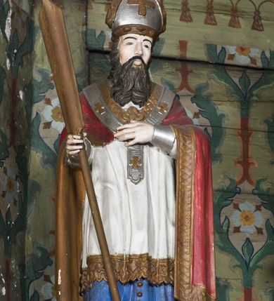 Zdjęcie nr 12: Nastawa ołtarzowa na planie półowalu uzyskała architektoniczną, jednokondygnacyjną strukturę ze zwieńczeniem. Jednoosiowe retabulum flankowane bramkami, na których ustawiono figury św. Wojciecha i św. Stanisława. Stipes ołtarz ujmuje drewniana prostopadłościenna obudowa podtrzymująca drewnianą mensą z portatylem. Drewniane antependium ujęte zostało czworoboczną, profilowaną ramą z płaskorzeźbionym i złoconym barankiem apokaliptycznym leżącym na księdze. Na mensie ustawiono współczesne tabernakulum pancerne w formie prostopadłościennej skrzynki. Kondygnacja retabulum ujęta została dwiema parami pilastrów zwróconych delikatnie do wewnątrz oraz silnie wysuniętą do przodu parą kolumn o kapitelach kompozytowych oraz dwie wolutowe konsole. Podpory dźwigają pełne belkowanie wsparte na impostach, o wklęsło-wypukłej linii. Nad polem środkowym widoczne jest połączenie wyłącznie gzymsem przyjmującym formę łuku falistego, wyłamane na osiach podpór. Na środku belkowania umieszczono kartusz, od którego odchodzą dwie girland kwiatowe. Kondygnacje ujmują zredukowane do wici akantowej uszaki. W polu środkowym usytuowano obraz św. Wawrzyńca ujęty profilowaną ramą w formie stojącego prostokąta zamkniętego łukiem nadwieszonym. Zwieńczenie nastawy uzyskało formę leżącego prostokąta flankowanego dwoma spływami wolutowymi opadającymi na belkowanie. Obie woluty dźwigają niepełne, wklęsło-wypukłe belkowanie przyjmujące nad polem formę łuku falistego. W centrum zwieńczenia umieszczono rzeźbioną grupę ze sceną koronacji Marii w srebrzonych obłokach z promieniami. Struktura nastawy jest polichromowana w kolorze białym, kolumny, konsole, profile i ornamentyka pierwotnie były złocone.