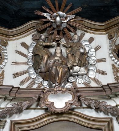 Zdjęcie nr 8: Nastawa ołtarzowa na planie półowalu uzyskała architektoniczną, jednokondygnacyjną strukturę ze zwieńczeniem. Jednoosiowe retabulum flankowane bramkami, na których ustawiono figury św. Wojciecha i św. Stanisława. Stipes ołtarz ujmuje drewniana prostopadłościenna obudowa podtrzymująca drewnianą mensą z portatylem. Drewniane antependium ujęte zostało czworoboczną, profilowaną ramą z płaskorzeźbionym i złoconym barankiem apokaliptycznym leżącym na księdze. Na mensie ustawiono współczesne tabernakulum pancerne w formie prostopadłościennej skrzynki. Kondygnacja retabulum ujęta została dwiema parami pilastrów zwróconych delikatnie do wewnątrz oraz silnie wysuniętą do przodu parą kolumn o kapitelach kompozytowych oraz dwie wolutowe konsole. Podpory dźwigają pełne belkowanie wsparte na impostach, o wklęsło-wypukłej linii. Nad polem środkowym widoczne jest połączenie wyłącznie gzymsem przyjmującym formę łuku falistego, wyłamane na osiach podpór. Na środku belkowania umieszczono kartusz, od którego odchodzą dwie girland kwiatowe. Kondygnacje ujmują zredukowane do wici akantowej uszaki. W polu środkowym usytuowano obraz św. Wawrzyńca ujęty profilowaną ramą w formie stojącego prostokąta zamkniętego łukiem nadwieszonym. Zwieńczenie nastawy uzyskało formę leżącego prostokąta flankowanego dwoma spływami wolutowymi opadającymi na belkowanie. Obie woluty dźwigają niepełne, wklęsło-wypukłe belkowanie przyjmujące nad polem formę łuku falistego. W centrum zwieńczenia umieszczono rzeźbioną grupę ze sceną koronacji Marii w srebrzonych obłokach z promieniami. Struktura nastawy jest polichromowana w kolorze białym, kolumny, konsole, profile i ornamentyka pierwotnie były złocone.