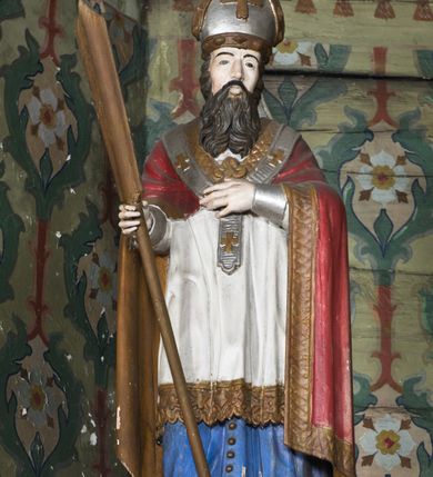 Zdjęcie nr 10: Nastawa ołtarzowa na planie półowalu uzyskała architektoniczną, jednokondygnacyjną strukturę ze zwieńczeniem. Jednoosiowe retabulum flankowane bramkami, na których ustawiono figury św. Wojciecha i św. Stanisława. Stipes ołtarz ujmuje drewniana prostopadłościenna obudowa podtrzymująca drewnianą mensą z portatylem. Drewniane antependium ujęte zostało czworoboczną, profilowaną ramą z płaskorzeźbionym i złoconym barankiem apokaliptycznym leżącym na księdze. Na mensie ustawiono współczesne tabernakulum pancerne w formie prostopadłościennej skrzynki. Kondygnacja retabulum ujęta została dwiema parami pilastrów zwróconych delikatnie do wewnątrz oraz silnie wysuniętą do przodu parą kolumn o kapitelach kompozytowych oraz dwie wolutowe konsole. Podpory dźwigają pełne belkowanie wsparte na impostach, o wklęsło-wypukłej linii. Nad polem środkowym widoczne jest połączenie wyłącznie gzymsem przyjmującym formę łuku falistego, wyłamane na osiach podpór. Na środku belkowania umieszczono kartusz, od którego odchodzą dwie girland kwiatowe. Kondygnacje ujmują zredukowane do wici akantowej uszaki. W polu środkowym usytuowano obraz św. Wawrzyńca ujęty profilowaną ramą w formie stojącego prostokąta zamkniętego łukiem nadwieszonym. Zwieńczenie nastawy uzyskało formę leżącego prostokąta flankowanego dwoma spływami wolutowymi opadającymi na belkowanie. Obie woluty dźwigają niepełne, wklęsło-wypukłe belkowanie przyjmujące nad polem formę łuku falistego. W centrum zwieńczenia umieszczono rzeźbioną grupę ze sceną koronacji Marii w srebrzonych obłokach z promieniami. Struktura nastawy jest polichromowana w kolorze białym, kolumny, konsole, profile i ornamentyka pierwotnie były złocone.