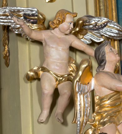 Zdjęcie nr 13: Nastawa ołtarzowa jest architektoniczna, jednoosiowa, jednokondygnacyjna ze zwieńczeniem, ustawiona na wysokim cokole. Ołtarz jest murowany, prostopadłościenny z marmurową mensą z portatylem. Trzy boki ołtarza ujmują malowane na płótnie obrazy w profilowanych, polichromowanych ramach. W polu antepedium znajduje się wyobrażenie architektonicznej nastawy z przedstawieniem baranka na ołtarzu, którą flankują sylwetki św. Piotra i św. Pawła.Tabernakulum ołtarza w formie metalowej skrzynki o wypukłym froncie i drewnianej obudowie w postaci wklęsłych boków zamkniętych parą pilastrów, których trzony przechodzą w spływy wolutowe. Podpory dźwigają profilowany gzyms przebiegający przez całą szerokość tabernakulum, nad frontem dekorowany lambrekinem. Metalowe drzwiczki mają kształt stojącego prostokąta zamkniętego łukiem półkolistym z aplikacjami w postaci kielicha z hostią w glorii, kłosami zbóż i winnego grona. Ponad drzwiczkami znajduje się kartusz z przedstawieniem pelikana. Na tabernakulum umiejscowiony jest tron wystawienia  w formie rzeźbionego ornamentalnego tła, flankowany przez parę rzeźbionych aniołów trzymających lichtarze. Retabulum ujęte jest parą opilastrowanych filarów i parą stojących przed nimi kolumn o kapitelach kompozytowych ustawionych pod kątem względem lica ołtarza. Podpory dźwigają wyłamujące się ponad nimi belkowanie z przerwanymi nad polem środkowym architrawem i fryzem. Zwieńczenie flankuje para spływów wolutowych, zamyka fragment wyłamanego na końcach gzymsu. Retabulum ujmuje para ażurowych, rocaille'owych uszaków, a w zwieńczeniu para figur adorujących aniołów. Trzony pilastrów zdobią rocaille'owe zwisy. W polu środkowym retabulum jest wnęka w formie stojącego prostokąta zamkniętego uskokowym, nadwieszonym łukiem półkolistym, ujęta profilowaną ramą. Wewnątrz znajduje się obraz Matki Boskiej z Dzieciątkiem. Powyżej, pośrodku belkowania umieszczono rocaille'owy kartusz z płaskorzeźbioną, zamkniętą koroną w polu. W zwieńczeniu jest obraz św. Józefa w profilowanej ramie w kształcie zbliżonym do stojącego prostokąta zamkniętego łukiem segmentowym z uskokiem oraz wklęsłymi dolnymi narożami. Szczyt ma formę rokokowego kartusza z malowanym okiem Opatrzności. Na zdobionych motywami rocaille'owymi wolutach spływów znajduje się para aniołów. 

Struktura ołtarza jest polichromowana w kolorze beżowym, trzony kolumn marmoryzowane, ornamentyka i profile złocone. 
