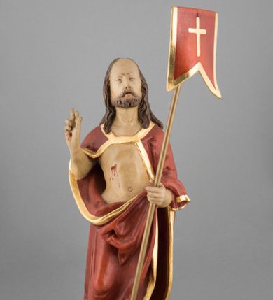 Zdjęcie nr 1: Rzeźba pełna, ustawiona na podstawie na planie nieregularnego koła przedstawia całopostaciowy wizerunek Chrystusa Zmartwychwstałego stojącego frontalnie, w kontrapoście, w lewej ręce trzymającego chorągiew paschalną, z prawą uniesioną w geście błogosławieństwa. Twarz jest szczupła, pociągła, o wysokim czole, delikatnie rzeźbionych rysach i wystających kościach policzkowych, niewielkich oczach zwróconych ku górze, prostym nosie i rozchylonych ustach, okolona krótką brodą skręconą w dwa pukle oraz falowanymi włosami opadającymi na ramiona. Jezus ubrany jest w czerwony płaszcz ze złotą lamówką, odsłaniający tors, zapięty na piersi, opadający na ramiona i plecy, zarzucony z przodu na lewe przedramię, przesłaniając partie nóg. Ciało jest szczupłe, o delikatnym modelunku z zaznaczonymi śladami męki. Polichromia naturalistyczna.