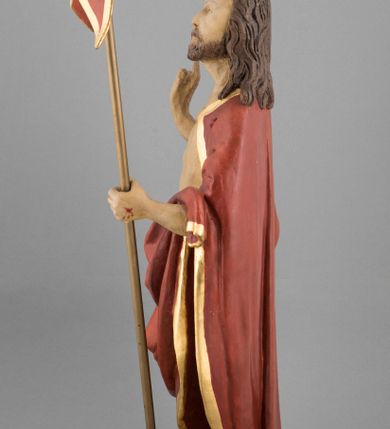 Zdjęcie nr 5: Rzeźba pełna, ustawiona na podstawie na planie nieregularnego koła przedstawia całopostaciowy wizerunek Chrystusa Zmartwychwstałego stojącego frontalnie, w kontrapoście, w lewej ręce trzymającego chorągiew paschalną, z prawą uniesioną w geście błogosławieństwa. Twarz jest szczupła, pociągła, o wysokim czole, delikatnie rzeźbionych rysach i wystających kościach policzkowych, niewielkich oczach zwróconych ku górze, prostym nosie i rozchylonych ustach, okolona krótką brodą skręconą w dwa pukle oraz falowanymi włosami opadającymi na ramiona. Jezus ubrany jest w czerwony płaszcz ze złotą lamówką, odsłaniający tors, zapięty na piersi, opadający na ramiona i plecy, zarzucony z przodu na lewe przedramię, przesłaniając partie nóg. Ciało jest szczupłe, o delikatnym modelunku z zaznaczonymi śladami męki. Polichromia naturalistyczna.