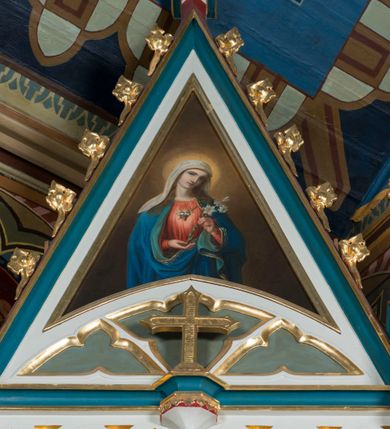 Zdjęcie nr 19: Ołtarz Najświętszego Serca Pana Jezusa uzyskał formę drewnianej i polichromowanej przyściennej struktury architektonicznej. Jest to założenie jednoosiowe i jednokondygnacyjne ze zwieńczeniem. Drewniana mensa wspiera się na prostopadłościennym drewnianym stipesie ołtarzowym flankowanym po bokach kolumienkami na wysokich cokolikach. Antepedium zostało podzielone obramionymi podłużnymi dwiema płycinami. Ich wewnętrzne krótsze boki są wklęsłe. W centrum pomiędzy płycinami znajduje się złocony czteroliść w owalu z wpisanym w środku krzyżem równoramiennym. Nastawa została ustawiona na zdwojonym cokole z przylegającym do niego na środku wielobocznym tabernakulum. Prostopadłościenne tabernakulum o ściętych narożach dekorowane jest płycinami ozdobionymi przenikającymi się ostrołukami z noskami. Drzwiczki zdobią litery alfa i omega. Górną część tabernakulum zamyka profilowany gzyms, natomiast dolną dekoruje pseudogotycki fryz z motywem czteroliścia wpisanego w romboidalną kratownicę. Podobny fryz znajduje się w dolnej cześć cokołu nastawy. Z kolei górną zdobią podłużne płyciny ze złoconą dekoracją maswerkową. Z cokołu wyrasta architektoniczna struktura utworzona z centralnej aediculi flankowanej parami kolumn o korynckich, złoconych kapitelach i czerwonych trzonach dekorowanych złotym ornamentem geometrycznym. Kolumny zostały ustawione na niewielkich postumentach. Podtrzymują one imposty z cokolikami z rozetami, z których wyrastają złocone, skręcone mniejsze kolumienki z fantazyjnymi kapitelami podtrzymującymi czworoboczne sterczyny przechodzące w pinakle zwieńczone kwiatonami. W dolnej części pomiędzy kolumnami zastosowano wydłużone płyciny zwieńczone trójbocznie z wpisanymi ostrołukami, wypełnionymi złoconym ornamentem astwerkowym. Natomiast w górnej części pomiędzy skręconymi kolumienkami oraz w tle arkady wieńczącej aediculę zastosowano płyciny dekorowane złoconymi ostrołukami z noskami. Ponad bocznymi płycinami wypiętrzono po bokach dwa mniejsze trójkątne szczyty zakończone pinaklami. Większy trójkątny szczyt, wypełniony obrazem z przedstawieniem Niepokalanego Serca Najświętszej Marii Panny, wznosi się nad centralną aediculą zakończoną ostrołukowo. W górnej części ostrołuk aediculi wypełnia ażurowy fantazyjny maswerk. W aediculi znajduje się obraz Najświętszego Serca Pana Jezusa, a na zasuwach obraz Matki Boskiej Różańcowej i św. Barbary. Nastawę po bokach flankują pełnoplastyczne figury św. Dominika oraz św. Katarzyny Sieneńskiej. Całość polichromowana jest w odcieniach seledynowej zieleni, rozbielonej czerwieni oraz błękintawej szarości. Partie ornamentów i profile płycin są złocone.