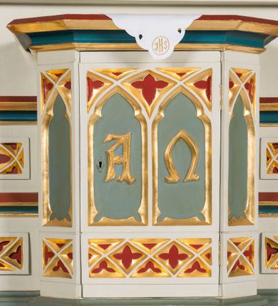 Zdjęcie nr 11: Ołtarz Najświętszego Serca Pana Jezusa uzyskał formę drewnianej i polichromowanej przyściennej struktury architektonicznej. Jest to założenie jednoosiowe i jednokondygnacyjne ze zwieńczeniem. Drewniana mensa wspiera się na prostopadłościennym drewnianym stipesie ołtarzowym flankowanym po bokach kolumienkami na wysokich cokolikach. Antepedium zostało podzielone obramionymi podłużnymi dwiema płycinami. Ich wewnętrzne krótsze boki są wklęsłe. W centrum pomiędzy płycinami znajduje się złocony czteroliść w owalu z wpisanym w środku krzyżem równoramiennym. Nastawa została ustawiona na zdwojonym cokole z przylegającym do niego na środku wielobocznym tabernakulum. Prostopadłościenne tabernakulum o ściętych narożach dekorowane jest płycinami ozdobionymi przenikającymi się ostrołukami z noskami. Drzwiczki zdobią litery alfa i omega. Górną część tabernakulum zamyka profilowany gzyms, natomiast dolną dekoruje pseudogotycki fryz z motywem czteroliścia wpisanego w romboidalną kratownicę. Podobny fryz znajduje się w dolnej cześć cokołu nastawy. Z kolei górną zdobią podłużne płyciny ze złoconą dekoracją maswerkową. Z cokołu wyrasta architektoniczna struktura utworzona z centralnej aediculi flankowanej parami kolumn o korynckich, złoconych kapitelach i czerwonych trzonach dekorowanych złotym ornamentem geometrycznym. Kolumny zostały ustawione na niewielkich postumentach. Podtrzymują one imposty z cokolikami z rozetami, z których wyrastają złocone, skręcone mniejsze kolumienki z fantazyjnymi kapitelami podtrzymującymi czworoboczne sterczyny przechodzące w pinakle zwieńczone kwiatonami. W dolnej części pomiędzy kolumnami zastosowano wydłużone płyciny zwieńczone trójbocznie z wpisanymi ostrołukami, wypełnionymi złoconym ornamentem astwerkowym. Natomiast w górnej części pomiędzy skręconymi kolumienkami oraz w tle arkady wieńczącej aediculę zastosowano płyciny dekorowane złoconymi ostrołukami z noskami. Ponad bocznymi płycinami wypiętrzono po bokach dwa mniejsze trójkątne szczyty zakończone pinaklami. Większy trójkątny szczyt, wypełniony obrazem z przedstawieniem Niepokalanego Serca Najświętszej Marii Panny, wznosi się nad centralną aediculą zakończoną ostrołukowo. W górnej części ostrołuk aediculi wypełnia ażurowy fantazyjny maswerk. W aediculi znajduje się obraz Najświętszego Serca Pana Jezusa, a na zasuwach obraz Matki Boskiej Różańcowej i św. Barbary. Nastawę po bokach flankują pełnoplastyczne figury św. Dominika oraz św. Katarzyny Sieneńskiej. Całość polichromowana jest w odcieniach seledynowej zieleni, rozbielonej czerwieni oraz błękintawej szarości. Partie ornamentów i profile płycin są złocone.