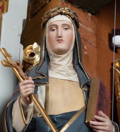 Zdjęcie nr 3: Pełnoplastyczna figura stojącej św. Katarzyny Sieneńskiej ustawiona została na niskim prostopadłościennym postumencie o ściętych narożach. Święta została przedstawiona w lekkim kontrapoście jako młoda kobieta. W uniesionej prawej ręce trzyma złocony krucyfiks, a  w lewej przyciśniętej do piersi zamknietą księgę. Ma owalną, pełną twarz o jasnej karnacji. Charakteryzują ją małe usta, prosty nos oraz wydatny podbródek. Katarzyna ubrana jest w biały habit dominikański z kremowym szkaplerzem, lamowanym złotą taśmą. Na ramionach ma narzucony ciemnoszary płaszcz lamowany przy krawędziach złotą taśmą. Na głowie ma zakonny kornet z podwiką i szaroczarny welon oraz złoconą koronę cierniową. 