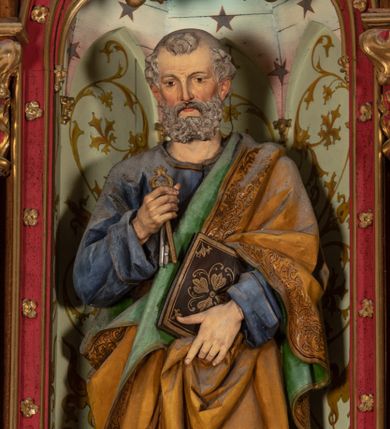 Zdjęcie nr 1: Pełnoplastyczna, polichromowana figura ustawiona na niewysokim, prostopadłościennym postumencie ukazuje św. Piotra Apostoła. Święty został przedstawiony frontalnie w nieznacznym kontrapoście jako starszy, siwiejący mężczyzna z krótką brodą. W lewej dłoni na wysokości pasa podtrzymuje zamkniętą księgę w ozdobnej oprawie, natomiast w prawej ręce zgiętej w łokciu przy piersi ma złoty i srebrny klucz. Święty ma pociągłą twarz o jasnej karnacji, rumiane policzki i wydane zakola na wysokim czole.  Spojrzenie jego ciemnych, zamyślonych oczu skierowane jest przed siebie. Apostoł ubrany jest w długą ciemnoniebieską tunikę odsłaniającą u spodu fragmenty bosych stóp. Przez lewe ramię ma przerzucony obszerny, obficie drapowany, żółty płaszcz z zieloną podszewką ze złotą lamówką. Na cokole widnieje złocona inskrypcja „Św(ięty) Piotr&quot;.