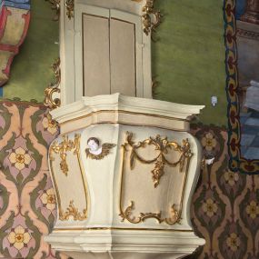 Zdjęcie nr 1: Ambona wisząca, przyścienna z baldachimem. Kosz czworoboczny o ściętych narożach, lekko wybrzuszony w górnej części. W polach płyciny utworzone z ornamentu rocaille oraz podwieszone festony roślinne; w narożach polichromowane i złocone uskrzydlone główki anielskie. U dołu kosza ambony cztery odwrócone woluty. Zaplecek ujęty pilastrami o gładkich trzonach z wolutami i festonami w górnej części oraz uszami utworzonymi z rocaille'ów. W zaplecku dwuskrzydłowe drzwi. Baldachim czworoboczny w formie belkowania o wklęsło-wypukłej linii z podwieszonym lambrekinem. W zwieńczeniu srebrzona gołębica Ducha Świętego na tle obłoków oraz glorii promienistej.

Struktura malowana w odcieniach bieli i różu; ornamenty złocone.