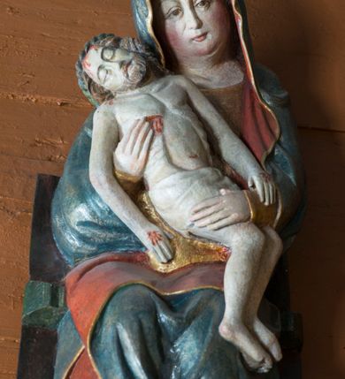 Zdjęcie nr 10: Pieta w Jawiszowicach reprezentuje Pietę w tzw. typie Pieta corpusculum. Przedstawiono tutaj pełnopostaciową figurę siedzącej Marii, trzymającą na kolanach martwe ciało Chrystusa. Matka Boska jest lekko pochylona w prawą stronę. Obiema rękami podtrzymuje na swoich kolanach Chrystusa, opartego o jej prawe przedramię. Prawą ręką trzyma go za bok, a lewą kładzie na jego udach. Ma owalną twarz o jasnej karnacji z wysokim czołem. Jej oczy są duże, wyraźne. Maria ma długi, prosty nos, czerwone usta, rumiane policzki i nieznacznie zaznaczone zmarszczki podkreślające jej cierpienie. Matka Boska odziana jest w złotą tunikę i ciemnobłękitny maforion z czerwonym podbiciem lamowany złotem, okrywający jej postać. Fałdy płaszcza są misowate, miękko rzeźbione. Spód szaty odsłania brunatne ciżmy. Martwy Chrystus jest wielkości dziecka. Jego ciało z odchyloną głową ułożone jest prawie schodkowo. Twarz z zamkniętymi oczami okala zarost oraz włosy. Na głowie ma koronę cierniową, spod której sączą się na czoło stróżki krwi. Krew cieknie także z przebitego boku. Biodra Chrystusa okrywa jasne, miękko drapowane perizonium.  
Rzeźba stoi na współczesnej, stylizowanej na gotycką pięciobocznej konsoli. Jej profilowany cokół podtrzymuje wspornik opleciony  srebrzystymi i złotymi liśćmi akantu. Krawędzie konsoli są pozłocone.