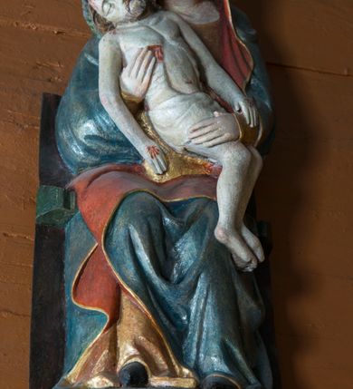 Zdjęcie nr 9: Pieta w Jawiszowicach reprezentuje Pietę w tzw. typie Pieta corpusculum. Przedstawiono tutaj pełnopostaciową figurę siedzącej Marii, trzymającą na kolanach martwe ciało Chrystusa. Matka Boska jest lekko pochylona w prawą stronę. Obiema rękami podtrzymuje na swoich kolanach Chrystusa, opartego o jej prawe przedramię. Prawą ręką trzyma go za bok, a lewą kładzie na jego udach. Ma owalną twarz o jasnej karnacji z wysokim czołem. Jej oczy są duże, wyraźne. Maria ma długi, prosty nos, czerwone usta, rumiane policzki i nieznacznie zaznaczone zmarszczki podkreślające jej cierpienie. Matka Boska odziana jest w złotą tunikę i ciemnobłękitny maforion z czerwonym podbiciem lamowany złotem, okrywający jej postać. Fałdy płaszcza są misowate, miękko rzeźbione. Spód szaty odsłania brunatne ciżmy. Martwy Chrystus jest wielkości dziecka. Jego ciało z odchyloną głową ułożone jest prawie schodkowo. Twarz z zamkniętymi oczami okala zarost oraz włosy. Na głowie ma koronę cierniową, spod której sączą się na czoło stróżki krwi. Krew cieknie także z przebitego boku. Biodra Chrystusa okrywa jasne, miękko drapowane perizonium.  
Rzeźba stoi na współczesnej, stylizowanej na gotycką pięciobocznej konsoli. Jej profilowany cokół podtrzymuje wspornik opleciony  srebrzystymi i złotymi liśćmi akantu. Krawędzie konsoli są pozłocone.