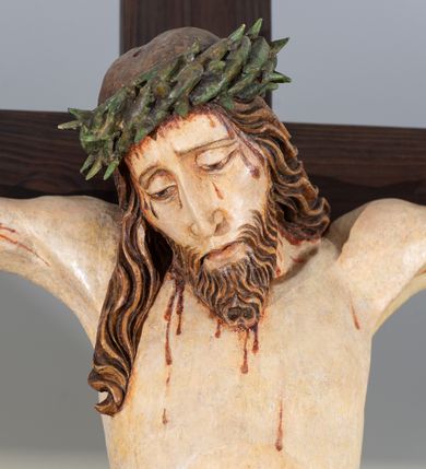 Zdjęcie nr 4: Na krucyfiksie przedstawiono ściętą z tyłu rzeźbioną figurę ukrzyżowanego Chrystusa. Jego ramiona ukazane zostały w lekkim zwisie, zaś układ ciała przyjmuje kształt litery „T”. Postać Ukrzyżowanego charakteryzuje się wydłużonymi proporcjami o wyraźnie zarysowanych mięśniach kończyn oraz zapadłą klatką piersiową. Głowa Jezusa jest przechylona na prawe ramię. Jego twarz jest pociągła o długim, prostym nosie, przymkniętych oczach i ustach wygiętych z kącikami skierowanymi do dołu. Okala ją brązowy zarost o szpicowatym zakończeniu. Włosy Zbawiciela są długie, kształtowane w falujące pukle, z pasmem opadającym na prawe ramię. Na głowie Jezus ma koronę cierniową, spod której spływają na twarz strugi krwi. Krew spływa także wzdłuż ramion, nóg i stóp. Na prawym boku zaznaczono broczącą ranę po włóczni. Ręce i nogi przytwierdzone są do krzyża za pomocą trzech gwoździ w kształcie czworobocznego graniastosłupa ściętego. Biodra Chrystusa przepasane zostały srebrzonym perizonium, przewiązanym na prawym biodrze ze zwisającym festonem wzdłuż prawego uda. Jest ono drapowane w szerokie fałdy wzdłuż przewiązania i na festonie. Ponad głową Zbawiciela widnieje późniejszy titulus z napisem „INRI”. Postać Chrystusa jest polichromowana, a perizonium srebrzone z widocznymi laserunkami.