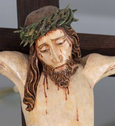 Zdjęcie nr 3: Na krucyfiksie przedstawiono ściętą z tyłu rzeźbioną figurę ukrzyżowanego Chrystusa. Jego ramiona ukazane zostały w lekkim zwisie, zaś układ ciała przyjmuje kształt litery „T”. Postać Ukrzyżowanego charakteryzuje się wydłużonymi proporcjami o wyraźnie zarysowanych mięśniach kończyn oraz zapadłą klatką piersiową. Głowa Jezusa jest przechylona na prawe ramię. Jego twarz jest pociągła o długim, prostym nosie, przymkniętych oczach i ustach wygiętych z kącikami skierowanymi do dołu. Okala ją brązowy zarost o szpicowatym zakończeniu. Włosy Zbawiciela są długie, kształtowane w falujące pukle, z pasmem opadającym na prawe ramię. Na głowie Jezus ma koronę cierniową, spod której spływają na twarz strugi krwi. Krew spływa także wzdłuż ramion, nóg i stóp. Na prawym boku zaznaczono broczącą ranę po włóczni. Ręce i nogi przytwierdzone są do krzyża za pomocą trzech gwoździ w kształcie czworobocznego graniastosłupa ściętego. Biodra Chrystusa przepasane zostały srebrzonym perizonium, przewiązanym na prawym biodrze ze zwisającym festonem wzdłuż prawego uda. Jest ono drapowane w szerokie fałdy wzdłuż przewiązania i na festonie. Ponad głową Zbawiciela widnieje późniejszy titulus z napisem „INRI”. Postać Chrystusa jest polichromowana, a perizonium srebrzone z widocznymi laserunkami.