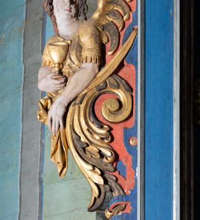 Zdjęcie nr 12: Retabulum św. Karola Boromeusza stanowi nastawę ze zwieńczeniem w formie architektonicznej, jednokondygnacyjną i jednoosiową. Wsparte jest na ośmiobocznej mensie spoczywającej na drewnianym stipesie w formie sarkofagowej, usytuowanym na niskim cokole. Boki stipesu ujmują złocone spływy wolutowe. Malowane antepedium ujęte jest przy górnej i dolnej krawędzi przez dwa pozłacane pasy z motywem małżowinowo-chrząstkowym. Predella retabulum w formie cokołu zawiera podłużne pole o nieregularnym kształcie z przedstawieniem Pokutnej procesji św. Karola Boromeusza w Mediolanie, ujęte po bokach dwoma prostokątnymi cokolikami, na których wspierają się pilastry retabulum. Retabulum jest oddzielone od predelli wąskim, spiętrzonym gzymsem, częściowo pozłacanym. Jego część środkową flankują dwa pilastry z głowicami kompozytowymi, wsparte na prostopadłościennych bazach, w których umieszczono prostokątne płyciny z motywem roślinnym. W centralnej części retabulum umieszczono obraz w formie stojącego prostokąta z przedstawieniem Modlitwy św. Karola Boromeusza. Po bokach nastawy znajdują się dwa uszaki uformowane z wici roślinno-kwiatowej, przedzielonej pośrodku płaskorzeźbionymi przedstawieniami aniołów. Ich zwrócone na zewnątrz sylwetki zostały wkomponowane motywy wolutowe. Anioł po lewej trzyma w prawej dłoni kielich mszalny, a anioł po prawej stronie ołtarza ma wzrok zwrócony w górę. Lewą, zgiętą w łokciu rękę trzyma na piersi, prawą ma wyprostowaną. Obraz jest ujęty w ramę o profilowanych bokach, zdobionych luźnymi motywami roślinnymi w formie stylizowanych liści akantu. Ponad nią widoczne jest profilowane belkowanie, załamane na osi pilastrów, wzbogacone na środku fryzem z motywami roślinnymi. W zwieńczeniu ołtarza umieszczono owalny obraz ze sceną Zamachu na św. Karola Boromeusza, ujęty ornamentem kartuszowym z elementami akantowymi i wolutowymi.