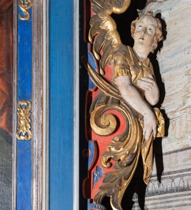 Zdjęcie nr 11: Retabulum św. Karola Boromeusza stanowi nastawę ze zwieńczeniem w formie architektonicznej, jednokondygnacyjną i jednoosiową. Wsparte jest na ośmiobocznej mensie spoczywającej na drewnianym stipesie w formie sarkofagowej, usytuowanym na niskim cokole. Boki stipesu ujmują złocone spływy wolutowe. Malowane antepedium ujęte jest przy górnej i dolnej krawędzi przez dwa pozłacane pasy z motywem małżowinowo-chrząstkowym. Predella retabulum w formie cokołu zawiera podłużne pole o nieregularnym kształcie z przedstawieniem Pokutnej procesji św. Karola Boromeusza w Mediolanie, ujęte po bokach dwoma prostokątnymi cokolikami, na których wspierają się pilastry retabulum. Retabulum jest oddzielone od predelli wąskim, spiętrzonym gzymsem, częściowo pozłacanym. Jego część środkową flankują dwa pilastry z głowicami kompozytowymi, wsparte na prostopadłościennych bazach, w których umieszczono prostokątne płyciny z motywem roślinnym. W centralnej części retabulum umieszczono obraz w formie stojącego prostokąta z przedstawieniem Modlitwy św. Karola Boromeusza. Po bokach nastawy znajdują się dwa uszaki uformowane z wici roślinno-kwiatowej, przedzielonej pośrodku płaskorzeźbionymi przedstawieniami aniołów. Ich zwrócone na zewnątrz sylwetki zostały wkomponowane motywy wolutowe. Anioł po lewej trzyma w prawej dłoni kielich mszalny, a anioł po prawej stronie ołtarza ma wzrok zwrócony w górę. Lewą, zgiętą w łokciu rękę trzyma na piersi, prawą ma wyprostowaną. Obraz jest ujęty w ramę o profilowanych bokach, zdobionych luźnymi motywami roślinnymi w formie stylizowanych liści akantu. Ponad nią widoczne jest profilowane belkowanie, załamane na osi pilastrów, wzbogacone na środku fryzem z motywami roślinnymi. W zwieńczeniu ołtarza umieszczono owalny obraz ze sceną Zamachu na św. Karola Boromeusza, ujęty ornamentem kartuszowym z elementami akantowymi i wolutowymi.