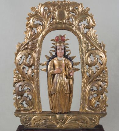 Zdjęcie nr 1: Feretron uzyskał formę dwuczęściowej konstrukcji. Górną tworzy wydłużone, owalne obramienie z ażurowej wici akantowo-roślinnej, dekorowanej przy szczycie wydatną rozetą, przechodzące w ścięty po bokach postument, zdobiony na środku z jednej strony płaskorzeźbioną, uskrzydloną główką aniołka, a z drugiej trupią czaszką, którym towarzyszy wić roślinna. Obramienie przymocowane jest do brązowej podstawy w kształcie leżącego graniastosłupa przeprutego dwoma kwadratowymi otworami przeznaczonymi na zakładanie drążków procesyjnych. Obramienie ujmuje pełnoplastyczną rzeźbę dwustronną z przedstawieniem stojącej w lekkim kontrapoście Matki Boskiej w złotej, zamkniętej koronie na głowie. Na wysokości ramion otacza ją promienista mandorla. Na awersie Madonna na wysokości piersi ma złożone ręce do modlitwy. Jej twarz o jasnej karnacji jest pociągła. Ma prosty, wydatny nos i wąskie usta. Spod korony spływają dwa pasma brązowych włosów, układających się na ramionach okrytych złotym płaszczem. Jego poły równolegle wzdłuż postaci opadają ku ziemi, odsłaniając długą, czerwoną tunikę lamowaną pod szyją i przy rękawach złotą taśmą. Z kolei na rewersie Maria prawą rękę ma przyłożoną do piersi, a w lewej, wyciągniętej przed siebie, trzymała niezachowane berło. Także tu Madonna ma mocno pociągłą twarz o prostym nosie i wąskich ustach. Spływające spod korony brązowe włosy układają się na jej ramionach. Ubrana jest w złoty płaszcz, którego poły opadają wzdłuż jej postaci, odkrywając złoty gorset i sięgającą kolan spódnicę, pod którą widoczna jest długa, złota tunika.  

