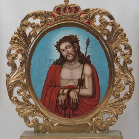 Zdjęcie nr 1: Pole obrazowe feretronu uzyskało kształt owalu ujętego w złoconą, ażurową ramę skomponowaną z liści akantu. Całość obramienia wieńczy zamknięta, korona z krzyżykiem na globie, wypełniona purpurą z obręczą naśladującą kameryzację. Na awersie w polu obrazowym feretronu przedstawiono Chrystusa Bolesnego w typie Ecce Homo. Postać ukazana została w półpostaci z głową lekko przechyloną w prawą stronę. Chrystus ma ręce związane w nadgarstkach. W prawej ręce trzyma trzcinę. Zarówno twarz, jak i tors otrzymały jasną karnację. Jego umęczone oblicze charakteryzuje prosty nos, szeroko otwarte oczy oraz wydatne, czerwone usta. Głowę okalają jasnobrązowe włosy, odsłaniające lewe ucho, które puklami opadają na ramiona. Wokół twarzy widoczny jest krótki zarost przechodzący w charakterystycznie zawiniętą podwójnie brodę. Na głowie ma małą koronę cierniową, spod której ciekną strużki krwi, widoczne na czole, skroniach, włosach, torsie i rękach. Chrystus na ramionach ma narzucony purpurowy płaszcz zakrywający prawe ramię, którego obie poły są zawinięte na wysokości skrępowanych dłoni. Jego postać otaczają delikatnie zaznaczone jasne promienie widoczne na jasnoniebieskim tle całego przedstawienia. Na rewersie pola obrazowego feretronu namalowano wizerunek Matki Boskiej Częstochowskiej. Madonna została ukazana frontalnie w półpostaci. Prawą ręką wskazuje na trzymane na lewym ramieniu Dzieciątko Jezus. Jej podłużną twarz o ciemnej karnacji charakteryzuje wydatny, prosty nos, migdałowe oczy, mięsiste usta oraz dwa równoległe cięcia widoczne na prawym policzku. Na głowie ma ciemnoniebieski maforion podbity czerwienią i lamowany ciemnoochrową taśmą, odsłaniający fragment szkarłatnej sukni na piersi oraz prawy jej rękaw. Pod szyją namalowano potrójny sznur pereł z zawieszonym na nim srebrnym krzyżykiem. Maria ma na głowie wysoką koronę o obłych sterczynach, dekorowaną imitacją pereł oraz kamieni szlachetnych. Dzieciątko zostało ujęte w trzech trzecich, z głową zwróconą w prawą stronę. Prawą rękę wznosi w geście błogosławieństwa, w lewej natomiast trzyma gruby kodeks Ewangelii w szkarłatnej okładce. Mały Jezus ma owalną twarz o ciemnej karnacji. Widoczny jest wydatny nos i usta oraz szeroko otwarte oczy. Ma na sobie szkarłatnoczerwoną tunikę zdobioną srebrnymi rozetkami i lamowaną ciemnoochrową grubą taśmą. Głowę Chrystusa wieńczy wysoka korona, kształtem i dekoracją zbliżona do korony Madonny. Głowy postaci otaczają złocistoochrowe nimby, poszerzone o czerwonożółty otok ze złotymi gwiazdami oraz dodatkowo malowane jasne promienie widoczne na jasnoniebieskim tle obrazu. 
