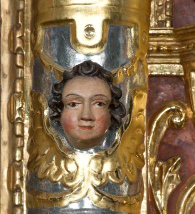 Zdjęcie nr 4: Ołtarz główny w Głębowicach otrzymał strukturę przyściennego, trójosiowego retabulum architektonicznego o dwóch kondygnacjach. Zaopatrzono go w predellę i zwieńczenie oraz dwa uszaki z boku zdobione herbem Starykoń i Jelita. Wisząc na ścianie wspiera się na dwóch masywnych, krótkich półkolumnach flankujących wejście do zakrystii. W środkowej części predelli widoczne jest wycięcie. Predellę po bokach ujmuje para konsoli wspierających wyłamujący się ponad nimi gzyms. Osie części środkowej nastawy ujęte są parami wolnostojących kolumn o kapitelach korynckich wspierających wyłamujące się ponad nimi belkowanie. Pole części środkowej nastawy ma kształt stojącego prostokąta zamkniętego nadwieszonym łukiem odcinkowym. Z kolei pola osi bocznych są artykułowane parą zamkniętych półkoliście niszy. Druga kondygnacja retabulum, będąca zarazem jego zwieńczeniem, została ujęta parą herm wspierających belkowanie przybierające formę łuku trójbocznego z ośmioboku. Po bokach widoczna jest para półkolistych, przerwanych przyczółków. Boki predelli ujęte zostały ulistnionymi wolutami, dodatkowo zdobionymi stylizowanymi motywami roślinno-kwiatowymi oraz motywem zwisu tkaniny z supłem. Konsole zdobione są liśćmi akantu oraz parą uskrzydlonych główek anielskich ze zwisami w formie pojedynczych kampanull. Po bokach predelli, na przedłużeniu zewnętrznych kolumn nastawy, podwieszono parę szyszek. Trzony kolumn zostały ozdobione w dolnej partii płaskorzeźbionymi, uskrzydlonymi główkami anielskimi, w górnej zewnętrzne – wicią winnej latorośli, zaś wewnętrzne motywem kandelabru. Osi boczne nastawy zostały ozdobione w dolnej partii ornamnetyką roślinną i parą główek anielskich ujętych motywami roślinnymi. Nisze dolnej kondygnacji wypełniono konchami, zdobionymi motywem ulistnionych rozetek. Z kolei trójboczne z ośmioboku konsole zostały ozdobione stylizowanymi liśćmi. W partii fryzu widoczna jest para mniejszych i większych uskrzydlonych główek anielskich. Drugą kondygnację - zwieńczenie, zostało ujęte parą herm z sylwetkami kobiecymi oraz parą uszaków o fantazyjnym wykroju z motywem maski lunarnej. Także fantazyjną formę z motywem głowy gryfa trzymającego w dziobie szarfę uzyskały uszaki w dolnej kondygnacji. W ich centrum widoczne są dwa owalne medaliony z herbem Starykoń i Jelita. W części środkowej nastawy znajduje się obraz Franciszka Lekszyckiego "Matka Boska Szkaplerzna wręcza szkaplerz św. Szymonowi Stockowi". Na zasuwie obraz "Matka Boska Różańcowa". Po bokach obrazu w niszach flankowanych kolumnami ustawiono rzeźbione wyobrażenie św. Marii Magdaleny i św. Katarzyny Aleksandryjskiej. W centrum drugiej kondygnacji-zwieńczeniu znajduje się obraz "Św. Maria Magdalena przed Ukrzyżowanym Chrystusem". Po bokach, na przyczółkach znajduje się para rzeźbionych stojących aniołów trzymających w dłoniach kartusze o fantazyjnych wykrojach. W kartuszu z prawej strony widnieje napis: "konserwacja 1973, 2016", a z lewej: "sancta scapularis". Na szczycie ołtarza trzy rzeźbione przedstawienia - bo bokach św. Piotra i św. Jana Ewangelisty, a po środku św. Krzysztofa. Struktura nastawy jest marmoryzowana w odcieniach różu i ceglastej czerwieni. Partie detalu architektonicznego i ornamentyka są złocone i srebrzone.