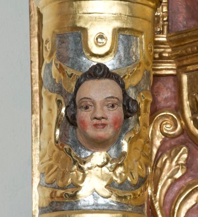 Zdjęcie nr 5: Ołtarz główny w Głębowicach otrzymał strukturę przyściennego, trójosiowego retabulum architektonicznego o dwóch kondygnacjach. Zaopatrzono go w predellę i zwieńczenie oraz dwa uszaki z boku zdobione herbem Starykoń i Jelita. Wisząc na ścianie wspiera się na dwóch masywnych, krótkich półkolumnach flankujących wejście do zakrystii. W środkowej części predelli widoczne jest wycięcie. Predellę po bokach ujmuje para konsoli wspierających wyłamujący się ponad nimi gzyms. Osie części środkowej nastawy ujęte są parami wolnostojących kolumn o kapitelach korynckich wspierających wyłamujące się ponad nimi belkowanie. Pole części środkowej nastawy ma kształt stojącego prostokąta zamkniętego nadwieszonym łukiem odcinkowym. Z kolei pola osi bocznych są artykułowane parą zamkniętych półkoliście niszy. Druga kondygnacja retabulum, będąca zarazem jego zwieńczeniem, została ujęta parą herm wspierających belkowanie przybierające formę łuku trójbocznego z ośmioboku. Po bokach widoczna jest para półkolistych, przerwanych przyczółków. Boki predelli ujęte zostały ulistnionymi wolutami, dodatkowo zdobionymi stylizowanymi motywami roślinno-kwiatowymi oraz motywem zwisu tkaniny z supłem. Konsole zdobione są liśćmi akantu oraz parą uskrzydlonych główek anielskich ze zwisami w formie pojedynczych kampanull. Po bokach predelli, na przedłużeniu zewnętrznych kolumn nastawy, podwieszono parę szyszek. Trzony kolumn zostały ozdobione w dolnej partii płaskorzeźbionymi, uskrzydlonymi główkami anielskimi, w górnej zewnętrzne – wicią winnej latorośli, zaś wewnętrzne motywem kandelabru. Osi boczne nastawy zostały ozdobione w dolnej partii ornamnetyką roślinną i parą główek anielskich ujętych motywami roślinnymi. Nisze dolnej kondygnacji wypełniono konchami, zdobionymi motywem ulistnionych rozetek. Z kolei trójboczne z ośmioboku konsole zostały ozdobione stylizowanymi liśćmi. W partii fryzu widoczna jest para mniejszych i większych uskrzydlonych główek anielskich. Drugą kondygnację - zwieńczenie, zostało ujęte parą herm z sylwetkami kobiecymi oraz parą uszaków o fantazyjnym wykroju z motywem maski lunarnej. Także fantazyjną formę z motywem głowy gryfa trzymającego w dziobie szarfę uzyskały uszaki w dolnej kondygnacji. W ich centrum widoczne są dwa owalne medaliony z herbem Starykoń i Jelita. W części środkowej nastawy znajduje się obraz Franciszka Lekszyckiego "Matka Boska Szkaplerzna wręcza szkaplerz św. Szymonowi Stockowi". Na zasuwie obraz "Matka Boska Różańcowa". Po bokach obrazu w niszach flankowanych kolumnami ustawiono rzeźbione wyobrażenie św. Marii Magdaleny i św. Katarzyny Aleksandryjskiej. W centrum drugiej kondygnacji-zwieńczeniu znajduje się obraz "Św. Maria Magdalena przed Ukrzyżowanym Chrystusem". Po bokach, na przyczółkach znajduje się para rzeźbionych stojących aniołów trzymających w dłoniach kartusze o fantazyjnych wykrojach. W kartuszu z prawej strony widnieje napis: "konserwacja 1973, 2016", a z lewej: "sancta scapularis". Na szczycie ołtarza trzy rzeźbione przedstawienia - bo bokach św. Piotra i św. Jana Ewangelisty, a po środku św. Krzysztofa. Struktura nastawy jest marmoryzowana w odcieniach różu i ceglastej czerwieni. Partie detalu architektonicznego i ornamentyka są złocone i srebrzone.