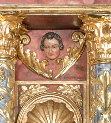 Zdjęcie nr 18: Ołtarz główny w Głębowicach otrzymał strukturę przyściennego, trójosiowego retabulum architektonicznego o dwóch kondygnacjach. Zaopatrzono go w predellę i zwieńczenie oraz dwa uszaki z boku zdobione herbem Starykoń i Jelita. Wisząc na ścianie wspiera się na dwóch masywnych, krótkich półkolumnach flankujących wejście do zakrystii. W środkowej części predelli widoczne jest wycięcie. Predellę po bokach ujmuje para konsoli wspierających wyłamujący się ponad nimi gzyms. Osie części środkowej nastawy ujęte są parami wolnostojących kolumn o kapitelach korynckich wspierających wyłamujące się ponad nimi belkowanie. Pole części środkowej nastawy ma kształt stojącego prostokąta zamkniętego nadwieszonym łukiem odcinkowym. Z kolei pola osi bocznych są artykułowane parą zamkniętych półkoliście niszy. Druga kondygnacja retabulum, będąca zarazem jego zwieńczeniem, została ujęta parą herm wspierających belkowanie przybierające formę łuku trójbocznego z ośmioboku. Po bokach widoczna jest para półkolistych, przerwanych przyczółków. Boki predelli ujęte zostały ulistnionymi wolutami, dodatkowo zdobionymi stylizowanymi motywami roślinno-kwiatowymi oraz motywem zwisu tkaniny z supłem. Konsole zdobione są liśćmi akantu oraz parą uskrzydlonych główek anielskich ze zwisami w formie pojedynczych kampanull. Po bokach predelli, na przedłużeniu zewnętrznych kolumn nastawy, podwieszono parę szyszek. Trzony kolumn zostały ozdobione w dolnej partii płaskorzeźbionymi, uskrzydlonymi główkami anielskimi, w górnej zewnętrzne – wicią winnej latorośli, zaś wewnętrzne motywem kandelabru. Osi boczne nastawy zostały ozdobione w dolnej partii ornamnetyką roślinną i parą główek anielskich ujętych motywami roślinnymi. Nisze dolnej kondygnacji wypełniono konchami, zdobionymi motywem ulistnionych rozetek. Z kolei trójboczne z ośmioboku konsole zostały ozdobione stylizowanymi liśćmi. W partii fryzu widoczna jest para mniejszych i większych uskrzydlonych główek anielskich. Drugą kondygnację - zwieńczenie, zostało ujęte parą herm z sylwetkami kobiecymi oraz parą uszaków o fantazyjnym wykroju z motywem maski lunarnej. Także fantazyjną formę z motywem głowy gryfa trzymającego w dziobie szarfę uzyskały uszaki w dolnej kondygnacji. W ich centrum widoczne są dwa owalne medaliony z herbem Starykoń i Jelita. W części środkowej nastawy znajduje się obraz Franciszka Lekszyckiego "Matka Boska Szkaplerzna wręcza szkaplerz św. Szymonowi Stockowi". Na zasuwie obraz "Matka Boska Różańcowa". Po bokach obrazu w niszach flankowanych kolumnami ustawiono rzeźbione wyobrażenie św. Marii Magdaleny i św. Katarzyny Aleksandryjskiej. W centrum drugiej kondygnacji-zwieńczeniu znajduje się obraz "Św. Maria Magdalena przed Ukrzyżowanym Chrystusem". Po bokach, na przyczółkach znajduje się para rzeźbionych stojących aniołów trzymających w dłoniach kartusze o fantazyjnych wykrojach. W kartuszu z prawej strony widnieje napis: "konserwacja 1973, 2016", a z lewej: "sancta scapularis". Na szczycie ołtarza trzy rzeźbione przedstawienia - bo bokach św. Piotra i św. Jana Ewangelisty, a po środku św. Krzysztofa. Struktura nastawy jest marmoryzowana w odcieniach różu i ceglastej czerwieni. Partie detalu architektonicznego i ornamentyka są złocone i srebrzone.