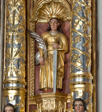 Zdjęcie nr 16: Ołtarz główny w Głębowicach otrzymał strukturę przyściennego, trójosiowego retabulum architektonicznego o dwóch kondygnacjach. Zaopatrzono go w predellę i zwieńczenie oraz dwa uszaki z boku zdobione herbem Starykoń i Jelita. Wisząc na ścianie wspiera się na dwóch masywnych, krótkich półkolumnach flankujących wejście do zakrystii. W środkowej części predelli widoczne jest wycięcie. Predellę po bokach ujmuje para konsoli wspierających wyłamujący się ponad nimi gzyms. Osie części środkowej nastawy ujęte są parami wolnostojących kolumn o kapitelach korynckich wspierających wyłamujące się ponad nimi belkowanie. Pole części środkowej nastawy ma kształt stojącego prostokąta zamkniętego nadwieszonym łukiem odcinkowym. Z kolei pola osi bocznych są artykułowane parą zamkniętych półkoliście niszy. Druga kondygnacja retabulum, będąca zarazem jego zwieńczeniem, została ujęta parą herm wspierających belkowanie przybierające formę łuku trójbocznego z ośmioboku. Po bokach widoczna jest para półkolistych, przerwanych przyczółków. Boki predelli ujęte zostały ulistnionymi wolutami, dodatkowo zdobionymi stylizowanymi motywami roślinno-kwiatowymi oraz motywem zwisu tkaniny z supłem. Konsole zdobione są liśćmi akantu oraz parą uskrzydlonych główek anielskich ze zwisami w formie pojedynczych kampanull. Po bokach predelli, na przedłużeniu zewnętrznych kolumn nastawy, podwieszono parę szyszek. Trzony kolumn zostały ozdobione w dolnej partii płaskorzeźbionymi, uskrzydlonymi główkami anielskimi, w górnej zewnętrzne – wicią winnej latorośli, zaś wewnętrzne motywem kandelabru. Osi boczne nastawy zostały ozdobione w dolnej partii ornamnetyką roślinną i parą główek anielskich ujętych motywami roślinnymi. Nisze dolnej kondygnacji wypełniono konchami, zdobionymi motywem ulistnionych rozetek. Z kolei trójboczne z ośmioboku konsole zostały ozdobione stylizowanymi liśćmi. W partii fryzu widoczna jest para mniejszych i większych uskrzydlonych główek anielskich. Drugą kondygnację - zwieńczenie, zostało ujęte parą herm z sylwetkami kobiecymi oraz parą uszaków o fantazyjnym wykroju z motywem maski lunarnej. Także fantazyjną formę z motywem głowy gryfa trzymającego w dziobie szarfę uzyskały uszaki w dolnej kondygnacji. W ich centrum widoczne są dwa owalne medaliony z herbem Starykoń i Jelita. W części środkowej nastawy znajduje się obraz Franciszka Lekszyckiego "Matka Boska Szkaplerzna wręcza szkaplerz św. Szymonowi Stockowi". Na zasuwie obraz "Matka Boska Różańcowa". Po bokach obrazu w niszach flankowanych kolumnami ustawiono rzeźbione wyobrażenie św. Marii Magdaleny i św. Katarzyny Aleksandryjskiej. W centrum drugiej kondygnacji-zwieńczeniu znajduje się obraz "Św. Maria Magdalena przed Ukrzyżowanym Chrystusem". Po bokach, na przyczółkach znajduje się para rzeźbionych stojących aniołów trzymających w dłoniach kartusze o fantazyjnych wykrojach. W kartuszu z prawej strony widnieje napis: "konserwacja 1973, 2016", a z lewej: "sancta scapularis". Na szczycie ołtarza trzy rzeźbione przedstawienia - bo bokach św. Piotra i św. Jana Ewangelisty, a po środku św. Krzysztofa. Struktura nastawy jest marmoryzowana w odcieniach różu i ceglastej czerwieni. Partie detalu architektonicznego i ornamentyka są złocone i srebrzone.