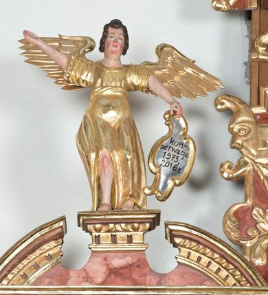 Zdjęcie nr 8: Ołtarz główny w Głębowicach otrzymał strukturę przyściennego, trójosiowego retabulum architektonicznego o dwóch kondygnacjach. Zaopatrzono go w predellę i zwieńczenie oraz dwa uszaki z boku zdobione herbem Starykoń i Jelita. Wisząc na ścianie wspiera się na dwóch masywnych, krótkich półkolumnach flankujących wejście do zakrystii. W środkowej części predelli widoczne jest wycięcie. Predellę po bokach ujmuje para konsoli wspierających wyłamujący się ponad nimi gzyms. Osie części środkowej nastawy ujęte są parami wolnostojących kolumn o kapitelach korynckich wspierających wyłamujące się ponad nimi belkowanie. Pole części środkowej nastawy ma kształt stojącego prostokąta zamkniętego nadwieszonym łukiem odcinkowym. Z kolei pola osi bocznych są artykułowane parą zamkniętych półkoliście niszy. Druga kondygnacja retabulum, będąca zarazem jego zwieńczeniem, została ujęta parą herm wspierających belkowanie przybierające formę łuku trójbocznego z ośmioboku. Po bokach widoczna jest para półkolistych, przerwanych przyczółków. Boki predelli ujęte zostały ulistnionymi wolutami, dodatkowo zdobionymi stylizowanymi motywami roślinno-kwiatowymi oraz motywem zwisu tkaniny z supłem. Konsole zdobione są liśćmi akantu oraz parą uskrzydlonych główek anielskich ze zwisami w formie pojedynczych kampanull. Po bokach predelli, na przedłużeniu zewnętrznych kolumn nastawy, podwieszono parę szyszek. Trzony kolumn zostały ozdobione w dolnej partii płaskorzeźbionymi, uskrzydlonymi główkami anielskimi, w górnej zewnętrzne – wicią winnej latorośli, zaś wewnętrzne motywem kandelabru. Osi boczne nastawy zostały ozdobione w dolnej partii ornamnetyką roślinną i parą główek anielskich ujętych motywami roślinnymi. Nisze dolnej kondygnacji wypełniono konchami, zdobionymi motywem ulistnionych rozetek. Z kolei trójboczne z ośmioboku konsole zostały ozdobione stylizowanymi liśćmi. W partii fryzu widoczna jest para mniejszych i większych uskrzydlonych główek anielskich. Drugą kondygnację - zwieńczenie, zostało ujęte parą herm z sylwetkami kobiecymi oraz parą uszaków o fantazyjnym wykroju z motywem maski lunarnej. Także fantazyjną formę z motywem głowy gryfa trzymającego w dziobie szarfę uzyskały uszaki w dolnej kondygnacji. W ich centrum widoczne są dwa owalne medaliony z herbem Starykoń i Jelita. W części środkowej nastawy znajduje się obraz Franciszka Lekszyckiego "Matka Boska Szkaplerzna wręcza szkaplerz św. Szymonowi Stockowi". Na zasuwie obraz "Matka Boska Różańcowa". Po bokach obrazu w niszach flankowanych kolumnami ustawiono rzeźbione wyobrażenie św. Marii Magdaleny i św. Katarzyny Aleksandryjskiej. W centrum drugiej kondygnacji-zwieńczeniu znajduje się obraz "Św. Maria Magdalena przed Ukrzyżowanym Chrystusem". Po bokach, na przyczółkach znajduje się para rzeźbionych stojących aniołów trzymających w dłoniach kartusze o fantazyjnych wykrojach. W kartuszu z prawej strony widnieje napis: "konserwacja 1973, 2016", a z lewej: "sancta scapularis". Na szczycie ołtarza trzy rzeźbione przedstawienia - bo bokach św. Piotra i św. Jana Ewangelisty, a po środku św. Krzysztofa. Struktura nastawy jest marmoryzowana w odcieniach różu i ceglastej czerwieni. Partie detalu architektonicznego i ornamentyka są złocone i srebrzone.