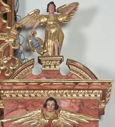 Zdjęcie nr 9: Ołtarz główny w Głębowicach otrzymał strukturę przyściennego, trójosiowego retabulum architektonicznego o dwóch kondygnacjach. Zaopatrzono go w predellę i zwieńczenie oraz dwa uszaki z boku zdobione herbem Starykoń i Jelita. Wisząc na ścianie wspiera się na dwóch masywnych, krótkich półkolumnach flankujących wejście do zakrystii. W środkowej części predelli widoczne jest wycięcie. Predellę po bokach ujmuje para konsoli wspierających wyłamujący się ponad nimi gzyms. Osie części środkowej nastawy ujęte są parami wolnostojących kolumn o kapitelach korynckich wspierających wyłamujące się ponad nimi belkowanie. Pole części środkowej nastawy ma kształt stojącego prostokąta zamkniętego nadwieszonym łukiem odcinkowym. Z kolei pola osi bocznych są artykułowane parą zamkniętych półkoliście niszy. Druga kondygnacja retabulum, będąca zarazem jego zwieńczeniem, została ujęta parą herm wspierających belkowanie przybierające formę łuku trójbocznego z ośmioboku. Po bokach widoczna jest para półkolistych, przerwanych przyczółków. Boki predelli ujęte zostały ulistnionymi wolutami, dodatkowo zdobionymi stylizowanymi motywami roślinno-kwiatowymi oraz motywem zwisu tkaniny z supłem. Konsole zdobione są liśćmi akantu oraz parą uskrzydlonych główek anielskich ze zwisami w formie pojedynczych kampanull. Po bokach predelli, na przedłużeniu zewnętrznych kolumn nastawy, podwieszono parę szyszek. Trzony kolumn zostały ozdobione w dolnej partii płaskorzeźbionymi, uskrzydlonymi główkami anielskimi, w górnej zewnętrzne – wicią winnej latorośli, zaś wewnętrzne motywem kandelabru. Osi boczne nastawy zostały ozdobione w dolnej partii ornamnetyką roślinną i parą główek anielskich ujętych motywami roślinnymi. Nisze dolnej kondygnacji wypełniono konchami, zdobionymi motywem ulistnionych rozetek. Z kolei trójboczne z ośmioboku konsole zostały ozdobione stylizowanymi liśćmi. W partii fryzu widoczna jest para mniejszych i większych uskrzydlonych główek anielskich. Drugą kondygnację - zwieńczenie, zostało ujęte parą herm z sylwetkami kobiecymi oraz parą uszaków o fantazyjnym wykroju z motywem maski lunarnej. Także fantazyjną formę z motywem głowy gryfa trzymającego w dziobie szarfę uzyskały uszaki w dolnej kondygnacji. W ich centrum widoczne są dwa owalne medaliony z herbem Starykoń i Jelita. W części środkowej nastawy znajduje się obraz Franciszka Lekszyckiego "Matka Boska Szkaplerzna wręcza szkaplerz św. Szymonowi Stockowi". Na zasuwie obraz "Matka Boska Różańcowa". Po bokach obrazu w niszach flankowanych kolumnami ustawiono rzeźbione wyobrażenie św. Marii Magdaleny i św. Katarzyny Aleksandryjskiej. W centrum drugiej kondygnacji-zwieńczeniu znajduje się obraz "Św. Maria Magdalena przed Ukrzyżowanym Chrystusem". Po bokach, na przyczółkach znajduje się para rzeźbionych stojących aniołów trzymających w dłoniach kartusze o fantazyjnych wykrojach. W kartuszu z prawej strony widnieje napis: "konserwacja 1973, 2016", a z lewej: "sancta scapularis". Na szczycie ołtarza trzy rzeźbione przedstawienia - bo bokach św. Piotra i św. Jana Ewangelisty, a po środku św. Krzysztofa. Struktura nastawy jest marmoryzowana w odcieniach różu i ceglastej czerwieni. Partie detalu architektonicznego i ornamentyka są złocone i srebrzone.