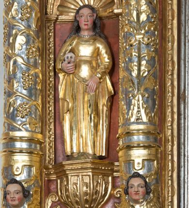 Zdjęcie nr 1: Święta Maria Magdalena, identyfikowana przez trzymaną ludzką czaszkę, została ukazana w całej postaci w nieznacznym kontrapoście. Rzeźba ma lekko zwróconą w lewo głowę. Święta ma owalną twarz o sumarycznym modelunku rysów i wyraźnie rumianych policzkach. Jej długie, lekko falowane, ciemnobrązowe włosy opadające na ramiona są założone za wydatne uszy. Maria Magdalena ubrana jest w długą, złoconą suknię z gorsetem oraz złocony, spięty pod szyją płaszcz. Na szyi widoczny jest krótki sznur pereł. Pod prawą pachą trzyma w uniesionej na wysokości talii prawej ręce ludzką czaszkę. Lewą zaś rękę wspiera na udzie. Figura nieznacznie ścięta z tyłu umieszczona jest w niszy pomiędzy dwiema kolumnami z prawej strony retabulum.