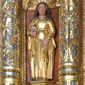 Zdjęcie nr 1: Święta Maria Magdalena, identyfikowana przez trzymaną ludzką czaszkę, została ukazana w całej postaci w nieznacznym kontrapoście. Rzeźba ma lekko zwróconą w lewo głowę. Święta ma owalną twarz o sumarycznym modelunku rysów i wyraźnie rumianych policzkach. Jej długie, lekko falowane, ciemnobrązowe włosy opadające na ramiona są założone za wydatne uszy. Maria Magdalena ubrana jest w długą, złoconą suknię z gorsetem oraz złocony, spięty pod szyją płaszcz. Na szyi widoczny jest krótki sznur pereł. Pod prawą pachą trzyma w uniesionej na wysokości talii prawej ręce ludzką czaszkę. Lewą zaś rękę wspiera na udzie. Figura nieznacznie ścięta z tyłu umieszczona jest w niszy pomiędzy dwiema kolumnami z prawej strony retabulum.