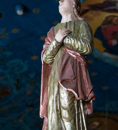 Zdjęcie nr 6: Grupa Ukrzyżowania składa się z pełnoplastycznych, całopostaciowych figur ustawionych na belce tęczowej. Pośrodku zamocowano polichromowany na ciemnobrązowo krzyż z realistycznie rzeźbioną figurą Chrystusa o plastycznie opracowanym modelunku muskulatury ciała. Postać do krzyża przytwierdzono za pomocą trzech gwoździ. Zbawiciel ma głowę pochyloną i złożoną na prawym barku. Posiada szeroką, owalną twarz o sumarycznie opracowanych rysach, półprzymknięte oczy, lekko rozchylone usta i krótki, ciemnobrązowy zarost. Długie, ciemnobrązowe, falowane włosy opadają mu na plecy i na prawy bark. Na głowie znajduje się zielona, cierniowa korona, spod której ciekną stróżki krwi. Nieproporcjonalnie długie ramiona ułożone zostały w płytkim, U-kształtnym zwisie z zaznaczonymi ścięgnami i żyłami na przedramionach. Dłonie o zaciśniętych palcach przybito dwoma gwoździami, spod których ciekną strużki krwi. Klatkę piersiową ukształtowano z wyraziście zaznaczoną linią żeber i raną w boku ze strugami krwi. Na biodrach umiejscowiono krótkie, złocone perizonium z festonem przy prawym boku. Jego zwichrowane draperie zostały ułożone horyzontalnie. Chrystus ma zgięte w kolanach nogi z założoną prawą stopą na lewą przybite jednym gwoździem. W górnej partii pionowej belki krzyża zawieszono biały titulus w formie banderoli z napisem: &quot;INRI&quot;. 
U stóp krzyża, po lewej stronie, na niskiej, prostopadłościennej podstawie, ustawiono rzeźbę klęczącej św. Marii Magdaleny. Święta jest zwrócona profilem w prawo. Jej owalną twarz charakteryzują sumarycznie opracowane rysy. Ma długie brązowe, lekko falowane włosy opadające na plecy. Ubrana jest w długą, srebrzystobłękitną, drobno fałdowaną suknię związaną srebrnym paskiem. Oburącz ujmuje pionową belkę krzyża. Tuż obok niej, na lewo, na niskiej, prostopadłościennej podstawie ustawiono figurę stojącej frontalnie Matki Boskiej Bolesnej. Jej nieznacznie odchyloną głowę charakteryzuje owalna, szeroka twarz o sumarycznie opracowanych rysach i wzroku skierowanym ku górze. Maria ubrana jest w długą srebrzyścieczerwoną suknię przewiązaną złotym paskiem i osłaniający głowę, plecy i prawe ramię, drobnofałdowany srebrzysty płaszcz. Ręce trzyma złożone w geście modlitwy. Po prawej stronie krzyża na niskiej, prostopadłościennej podstawie zamocowano stojącą figurę św. Jana Ewangelisty, ujętego frontalnie w nieznacznym kontrapoście. Święty ma lekko odchyloną do tyłu, zwróconą w trzech czwartych w lewo głowę. Charakteryzuje ją owalna, szeroka twarz o sumarycznie opracowanych rysach. Na plecy opadają mu długie, falowane, brązowe włosy. Jan ubrany jest w długą, srebrzystozieloną tunikę i przerzucony przez prawe ramię i podtrzymywany lewym przedramieniem złocistoochrowy płaszcz. Ręce trzyma skrzyżowane na piersiach. Z tyłu titulusa widnieje napis: Malował Jan i Ludwik, bracia Stankiewicze 1913. Napis widoczny jest także na górnej płaszczyźnie z tyłu krzyża: Malował 1913. 
Belka tęczowa jest prostopadłościenna, o profilowanych dolnych narożach. Polichromowano ją w odcieniach zieleni, czerwieni i żółci. Na środku widnieje flankowany parą złoconych krzyżyków złocony z przodu napis: + OTO BARANEK BOŻY KTÓRY GŁADZI GRZECHY ŚWIATA +; z tyłu: RENOVATUM A[nno] D[omini] 1913 + 1953 + 1983 + 2013