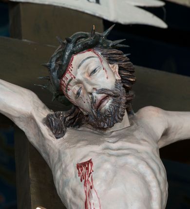 Zdjęcie nr 15: Grupa Ukrzyżowania składa się z pełnoplastycznych, całopostaciowych figur ustawionych na belce tęczowej. Pośrodku zamocowano polichromowany na ciemnobrązowo krzyż z realistycznie rzeźbioną figurą Chrystusa o plastycznie opracowanym modelunku muskulatury ciała. Postać do krzyża przytwierdzono za pomocą trzech gwoździ. Zbawiciel ma głowę pochyloną i złożoną na prawym barku. Posiada szeroką, owalną twarz o sumarycznie opracowanych rysach, półprzymknięte oczy, lekko rozchylone usta i krótki, ciemnobrązowy zarost. Długie, ciemnobrązowe, falowane włosy opadają mu na plecy i na prawy bark. Na głowie znajduje się zielona, cierniowa korona, spod której ciekną stróżki krwi. Nieproporcjonalnie długie ramiona ułożone zostały w płytkim, U-kształtnym zwisie z zaznaczonymi ścięgnami i żyłami na przedramionach. Dłonie o zaciśniętych palcach przybito dwoma gwoździami, spod których ciekną strużki krwi. Klatkę piersiową ukształtowano z wyraziście zaznaczoną linią żeber i raną w boku ze strugami krwi. Na biodrach umiejscowiono krótkie, złocone perizonium z festonem przy prawym boku. Jego zwichrowane draperie zostały ułożone horyzontalnie. Chrystus ma zgięte w kolanach nogi z założoną prawą stopą na lewą przybite jednym gwoździem. W górnej partii pionowej belki krzyża zawieszono biały titulus w formie banderoli z napisem: "INRI". 
U stóp krzyża, po lewej stronie, na niskiej, prostopadłościennej podstawie, ustawiono rzeźbę klęczącej św. Marii Magdaleny. Święta jest zwrócona profilem w prawo. Jej owalną twarz charakteryzują sumarycznie opracowane rysy. Ma długie brązowe, lekko falowane włosy opadające na plecy. Ubrana jest w długą, srebrzystobłękitną, drobno fałdowaną suknię związaną srebrnym paskiem. Oburącz ujmuje pionową belkę krzyża. Tuż obok niej, na lewo, na niskiej, prostopadłościennej podstawie ustawiono figurę stojącej frontalnie Matki Boskiej Bolesnej. Jej nieznacznie odchyloną głowę charakteryzuje owalna, szeroka twarz o sumarycznie opracowanych rysach i wzroku skierowanym ku górze. Maria ubrana jest w długą srebrzyścieczerwoną suknię przewiązaną złotym paskiem i osłaniający głowę, plecy i prawe ramię, drobnofałdowany srebrzysty płaszcz. Ręce trzyma złożone w geście modlitwy. Po prawej stronie krzyża na niskiej, prostopadłościennej podstawie zamocowano stojącą figurę św. Jana Ewangelisty, ujętego frontalnie w nieznacznym kontrapoście. Święty ma lekko odchyloną do tyłu, zwróconą w trzech czwartych w lewo głowę. Charakteryzuje ją owalna, szeroka twarz o sumarycznie opracowanych rysach. Na plecy opadają mu długie, falowane, brązowe włosy. Jan ubrany jest w długą, srebrzystozieloną tunikę i przerzucony przez prawe ramię i podtrzymywany lewym przedramieniem złocistoochrowy płaszcz. Ręce trzyma skrzyżowane na piersiach. Z tyłu titulusa widnieje napis: Malował Jan i Ludwik, bracia Stankiewicze 1913. Napis widoczny jest także na górnej płaszczyźnie z tyłu krzyża: Malował 1913. 
Belka tęczowa jest prostopadłościenna, o profilowanych dolnych narożach. Polichromowano ją w odcieniach zieleni, czerwieni i żółci. Na środku widnieje flankowany parą złoconych krzyżyków złocony z przodu napis: + OTO BARANEK BOŻY KTÓRY GŁADZI GRZECHY ŚWIATA +; z tyłu: RENOVATUM A[nno] D[omini] 1913 + 1953 + 1983 + 2013