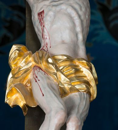 Zdjęcie nr 13: Grupa Ukrzyżowania składa się z pełnoplastycznych, całopostaciowych figur ustawionych na belce tęczowej. Pośrodku zamocowano polichromowany na ciemnobrązowo krzyż z realistycznie rzeźbioną figurą Chrystusa o plastycznie opracowanym modelunku muskulatury ciała. Postać do krzyża przytwierdzono za pomocą trzech gwoździ. Zbawiciel ma głowę pochyloną i złożoną na prawym barku. Posiada szeroką, owalną twarz o sumarycznie opracowanych rysach, półprzymknięte oczy, lekko rozchylone usta i krótki, ciemnobrązowy zarost. Długie, ciemnobrązowe, falowane włosy opadają mu na plecy i na prawy bark. Na głowie znajduje się zielona, cierniowa korona, spod której ciekną stróżki krwi. Nieproporcjonalnie długie ramiona ułożone zostały w płytkim, U-kształtnym zwisie z zaznaczonymi ścięgnami i żyłami na przedramionach. Dłonie o zaciśniętych palcach przybito dwoma gwoździami, spod których ciekną strużki krwi. Klatkę piersiową ukształtowano z wyraziście zaznaczoną linią żeber i raną w boku ze strugami krwi. Na biodrach umiejscowiono krótkie, złocone perizonium z festonem przy prawym boku. Jego zwichrowane draperie zostały ułożone horyzontalnie. Chrystus ma zgięte w kolanach nogi z założoną prawą stopą na lewą przybite jednym gwoździem. W górnej partii pionowej belki krzyża zawieszono biały titulus w formie banderoli z napisem: "INRI". 
U stóp krzyża, po lewej stronie, na niskiej, prostopadłościennej podstawie, ustawiono rzeźbę klęczącej św. Marii Magdaleny. Święta jest zwrócona profilem w prawo. Jej owalną twarz charakteryzują sumarycznie opracowane rysy. Ma długie brązowe, lekko falowane włosy opadające na plecy. Ubrana jest w długą, srebrzystobłękitną, drobno fałdowaną suknię związaną srebrnym paskiem. Oburącz ujmuje pionową belkę krzyża. Tuż obok niej, na lewo, na niskiej, prostopadłościennej podstawie ustawiono figurę stojącej frontalnie Matki Boskiej Bolesnej. Jej nieznacznie odchyloną głowę charakteryzuje owalna, szeroka twarz o sumarycznie opracowanych rysach i wzroku skierowanym ku górze. Maria ubrana jest w długą srebrzyścieczerwoną suknię przewiązaną złotym paskiem i osłaniający głowę, plecy i prawe ramię, drobnofałdowany srebrzysty płaszcz. Ręce trzyma złożone w geście modlitwy. Po prawej stronie krzyża na niskiej, prostopadłościennej podstawie zamocowano stojącą figurę św. Jana Ewangelisty, ujętego frontalnie w nieznacznym kontrapoście. Święty ma lekko odchyloną do tyłu, zwróconą w trzech czwartych w lewo głowę. Charakteryzuje ją owalna, szeroka twarz o sumarycznie opracowanych rysach. Na plecy opadają mu długie, falowane, brązowe włosy. Jan ubrany jest w długą, srebrzystozieloną tunikę i przerzucony przez prawe ramię i podtrzymywany lewym przedramieniem złocistoochrowy płaszcz. Ręce trzyma skrzyżowane na piersiach. Z tyłu titulusa widnieje napis: Malował Jan i Ludwik, bracia Stankiewicze 1913. Napis widoczny jest także na górnej płaszczyźnie z tyłu krzyża: Malował 1913. 
Belka tęczowa jest prostopadłościenna, o profilowanych dolnych narożach. Polichromowano ją w odcieniach zieleni, czerwieni i żółci. Na środku widnieje flankowany parą złoconych krzyżyków złocony z przodu napis: + OTO BARANEK BOŻY KTÓRY GŁADZI GRZECHY ŚWIATA +; z tyłu: RENOVATUM A[nno] D[omini] 1913 + 1953 + 1983 + 2013