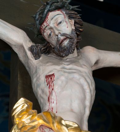 Zdjęcie nr 12: Grupa Ukrzyżowania składa się z pełnoplastycznych, całopostaciowych figur ustawionych na belce tęczowej. Pośrodku zamocowano polichromowany na ciemnobrązowo krzyż z realistycznie rzeźbioną figurą Chrystusa o plastycznie opracowanym modelunku muskulatury ciała. Postać do krzyża przytwierdzono za pomocą trzech gwoździ. Zbawiciel ma głowę pochyloną i złożoną na prawym barku. Posiada szeroką, owalną twarz o sumarycznie opracowanych rysach, półprzymknięte oczy, lekko rozchylone usta i krótki, ciemnobrązowy zarost. Długie, ciemnobrązowe, falowane włosy opadają mu na plecy i na prawy bark. Na głowie znajduje się zielona, cierniowa korona, spod której ciekną stróżki krwi. Nieproporcjonalnie długie ramiona ułożone zostały w płytkim, U-kształtnym zwisie z zaznaczonymi ścięgnami i żyłami na przedramionach. Dłonie o zaciśniętych palcach przybito dwoma gwoździami, spod których ciekną strużki krwi. Klatkę piersiową ukształtowano z wyraziście zaznaczoną linią żeber i raną w boku ze strugami krwi. Na biodrach umiejscowiono krótkie, złocone perizonium z festonem przy prawym boku. Jego zwichrowane draperie zostały ułożone horyzontalnie. Chrystus ma zgięte w kolanach nogi z założoną prawą stopą na lewą przybite jednym gwoździem. W górnej partii pionowej belki krzyża zawieszono biały titulus w formie banderoli z napisem: "INRI". 
U stóp krzyża, po lewej stronie, na niskiej, prostopadłościennej podstawie, ustawiono rzeźbę klęczącej św. Marii Magdaleny. Święta jest zwrócona profilem w prawo. Jej owalną twarz charakteryzują sumarycznie opracowane rysy. Ma długie brązowe, lekko falowane włosy opadające na plecy. Ubrana jest w długą, srebrzystobłękitną, drobno fałdowaną suknię związaną srebrnym paskiem. Oburącz ujmuje pionową belkę krzyża. Tuż obok niej, na lewo, na niskiej, prostopadłościennej podstawie ustawiono figurę stojącej frontalnie Matki Boskiej Bolesnej. Jej nieznacznie odchyloną głowę charakteryzuje owalna, szeroka twarz o sumarycznie opracowanych rysach i wzroku skierowanym ku górze. Maria ubrana jest w długą srebrzyścieczerwoną suknię przewiązaną złotym paskiem i osłaniający głowę, plecy i prawe ramię, drobnofałdowany srebrzysty płaszcz. Ręce trzyma złożone w geście modlitwy. Po prawej stronie krzyża na niskiej, prostopadłościennej podstawie zamocowano stojącą figurę św. Jana Ewangelisty, ujętego frontalnie w nieznacznym kontrapoście. Święty ma lekko odchyloną do tyłu, zwróconą w trzech czwartych w lewo głowę. Charakteryzuje ją owalna, szeroka twarz o sumarycznie opracowanych rysach. Na plecy opadają mu długie, falowane, brązowe włosy. Jan ubrany jest w długą, srebrzystozieloną tunikę i przerzucony przez prawe ramię i podtrzymywany lewym przedramieniem złocistoochrowy płaszcz. Ręce trzyma skrzyżowane na piersiach. Z tyłu titulusa widnieje napis: Malował Jan i Ludwik, bracia Stankiewicze 1913. Napis widoczny jest także na górnej płaszczyźnie z tyłu krzyża: Malował 1913. 
Belka tęczowa jest prostopadłościenna, o profilowanych dolnych narożach. Polichromowano ją w odcieniach zieleni, czerwieni i żółci. Na środku widnieje flankowany parą złoconych krzyżyków złocony z przodu napis: + OTO BARANEK BOŻY KTÓRY GŁADZI GRZECHY ŚWIATA +; z tyłu: RENOVATUM A[nno] D[omini] 1913 + 1953 + 1983 + 2013