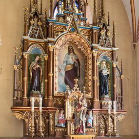 Zdjęcie nr 1: Jednokondygnacyjny i trójosiowy ołtarz ze zwieńczeniem uzyskał architektoniczną, bejcowaną i lakierowaną strukturę z partiami detalu i ornamentyką polichromowaną w kolorze czerwonym i niebieskim. Stipes ołtarzowy przyjął kształt prostopadłościanu z drewnianą mensą. Jego przód zdobią trzy pola z czworobocznymi płycinami ujętymi w złocone, profilowane ramki, rozdzielone kolumienkami z kapitelami korynckimi, ustawione na wysokich cokolikach z uskokiem. Środkową płaszczyznę dekoruje płaskorzeźbione i złocone przedstawienie Boskiego Serca w promienistej glorii z girlandą różaną. W dwóch pozostałych umieszczono płaskorzeźbione i złocone splecione litery Alfa i Omega oraz znak "Chi-Ro". Za ołtarzem rozpościera się wysoki cokół z parą niszy o konsolach zdobionych winną latoroślą. Na nim wspiera się predella nastawy dekorowana trójlistnymi arkadkami wspartymi na kolumienkach o złoconych korynckich kapitelach. W polach arkad umieszczono płaskorzeźbione i złocone przedstawienia stylizowanego kwiatu lilii. Na końcach predelli umieszczono ornament akantowy. Pośrodku predelli wkomponowano tabernakulum z tronem wystawienia. Tabernakulum uzyskało kształt prostopadłościennej szafki flankowanej parą złoconych kolumienek wspierających wyłamujący się ponad nimi gzyms. Dwuskrzydłowe drzwiczki zdobią płaskorzeźbione, złocone kłosy zbóż. Tabernakulum wieńczy złocony tron wystawienia w formie baldachimu wspartego na czterech kolumienkach, zamkniętego trzema ściankami z ośmioboku. Z kolei baldachim wieńczy ażurowa wimperga i para pinakli zdobione czołgankami i kwiatonami. Całość flankuje para prostopadłościennych cokołów zdobionych złoconym ornamentem, z dwoma figurami przyklękających na jednym kolanie aniołów z rękoma złożonymi w geście modlitewnym, ubranych w błękitno-różowe tuniki i dalmatyki. Każda z osi retabulum ujęta została parą kolumienek wspierających częściowo przerwane, wyłamujące się ponad nimi belkowanie. Gzyms w części środkowej uzyskał formę wimpergi. Retabulum po bokach zostało ujęte parą ażurowych uszaków z pojedynczymi kolumienkami o skręconych trzonach, zwieńczonych pojedynczymi pinaklami. Część środkowa zwieńczenia została ustawiona na cokole o zryzalitowanych bokach zwieńczonych parą pinakli. W szczycie usytuowano wsparty na parze kolumienek ażurowy baldachim z alternacji wimperg i pinakli, z wysokim, ażurowym pinaklem pośrodku. Nad osiami bocznymi retabulum usytuowano formy pary niewielkich kapliczek, których kolumienki wspierają wieńczące je duże, ażurowe pinakle oraz wimpergi flankowane parami mniejszych pinakli. Kapliczki ujęte są parami ażurowych wimperg u dołu oraz parami wysokich pinakli po bokach. Pinakle i wimpergi całej nastawy zdobione są złoconymi czołgankami i kwiatonami. Pole osi środkowej retabulum uzyskało formę płytkiej wnęki w kształcie stojącego prostokąta zamkniętego łukiem półkolistym z arkaturą. Ujmuje go profilowana, złocona rama zdobiona złoconą wicią winnej latorośli na ciemnoczerwonym tle. W środku umieszczono obraz Najświętsze Serce Pana Jezusa. Pola osi bocznych nastawy uzyskały formę trójbocznych niszy w kształcie stojących prostokątów zamkniętych łukiem ostrym o krawędzi zdobionej ażurowym ornamentem. Ścianki niszy pokrywa malowany, złocony astwerk na jasnozielonym tle, natomiast ich konchy błękit. Na ośmiobocznych postumentach zdobionych ornamentem ustawiono rzeźby świętych z podpisami. Z lewej strony znalazła się św. Teresa od Dzieciątka Jezus, a z prawej św. Małgorzata Alacoque. W zwieńczeniu, pośrodku, pod baldachimem umieszczono rzeźbę Chrystusa Dobrego Pasterza. Natomiast w kapliczkach po bokach parę figurek stojących aniołków ze złożonymi w geście modlitewnym rękoma.

