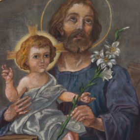 Zdjęcie nr 1: Pole obrazowe o lekko wklęsłych bokach, podstawie i dolnych narożach, zamknięte wklęsło-wypukłym łukiem uskokowym, ujęte profilowaną, złoconą ramą, w środku przedstawienie św. Józefa. Święty został przedstawiony w ujęciu półpostaciowym, nieznacznie zwrócony w lewo, z lekko odchyloną głową w trzech czwartych skierowaną w prawo. Pociągłą twarz charakteryzują delikatne rysy i krótki, brązowy zarost. Brązowe, falowane włosy sięgają szyi, a wokół głowy aureola. Święty ubrany jest w błękitno-fioletową suknię z długimi, szerokimi rękawami. W lewej dłoni ma kwiat lilii, a prawą podtrzymuje siedzące na strugnicy Dzieciątko Jezus w trzech czwartych zwrócone w prawo. Owalną twarz charakteryzują delikatne, dziecięce rysy, a  falowane, blond włosy sięgają szyi. Głowę Dzieciątka ujmuje świetlisty nimb krzyżowy, zaś sylwetkę osłania obszerny, biały płaszcz przerzucony przez lewe ramię. Lewa ręka i prawa noga Jezusa wyciągnięte są do przodu, a prawa ręka uniesiona w geście błogosławieństwa. Tuż za św. Józefem, po prawej stronie kompozycji, widoczne są wsparte o ścianę deski. Tło obrazu jest jednolite, szarobrązowe.