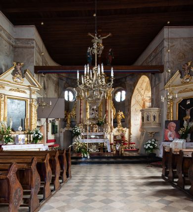 Zdjęcie nr 80: Kościół orientowany, murowany, jednonawowy z węższym prezbiterium zakończonym półkolistą absydą. Przy prezbiterium od północy znajduje się zakrystia, od południa kwadratowa kaplica św. Anny, a przy nawie od południa kruchta. Wnętrze kościoła nakryte jest nowym stropem, natomiast w kaplicy znajduje się sklepienie krzyżowo-żebrowe. Fasada zachodnia ujęta jest na narożnikach skośnymi szkarpami i zwieńczona schodkowym szczytem, podobnie zwieńczona jest kruchta południowa. Portal zachodni kamienny, z belkowaniem wspartym na dwóch liściastych konsolach ponad którymi edikula z płaskorzeźbionym krucyfiksem i klęczącymi postaciami męskimi. Na belkowaniu znajdują się dwa kartusze z herbami: po lewej herb Bończa, a nad nim litery „I” oraz „T”, a na prawo herb Szreniawa i litery „B” i „T”. Portal kruchty południowej jest również kamienny, podobny do zachodniego z inskrypcją: „IN LAVDEM ET GL[ORI]AM DEI O[MN]IP[OTENTIS] HO[NO]RE[M] / B(EATE) M(ARIAE) S(ANCTAE) V(IRGINIS) S(ANCTUS) AEGIDY ET OM(NIUM) SS. FIR. REGNÃTE [TERTIO] SIGISM[UN]DO / REGE POL[ONIAE] Z[?] HEMO[?] EP[ISCOP]O CRAC(OVIENSIS) BERN[AR]DO MACIEIOWSKI / NOVIT[ER] CAR[DINA]LI CRA[COVIENSE] DEI FACTO INTERI[M] PLEBA[N]O R[E]V[EREN]DO SEB(ASTIANO) / NAGRODIO A I SYRADIA PHI[LOSOPHI]AE DOCTORE COLLEG[I]A [MA]IORE / S. T(HEOLOGIAE) PVBLICO PROFES(SORE) PRAEP[OSI]TO S(ANCTA) AN(NAE) CRAC[OVIAE] DECIMARVM / ET FVNDI ECCL(ESIA)E HVIVS P[OST] IVRIS STREPITV(M) RESTITV / TORE ANNO OCTAVO PLEBANAT[U]S SVI. TEMPLVM HO(C) / [ dwa wiersze skute] DE' / NOWO AEDIFICATVM. ET. CONSTRVCTVM. ADIVTORIO / QVORVNDÃ ANNO D[OMINI] MDCIIII MENSE SEPTEMB[RE]”. Od południa świątyni umieszczone są trzy otwory okienne w kształcie stojących prostokątów, zamkniętych łukiem półkolistym, a w prezbiterium dwa małe okrągłe okna. Kościół nakryty jest dwoma dwuspadowymi dachami, nad prezbiterium nieco niższym, nad nawą zwieńczonym wąską i wysoką sygnaturką na dzwon. Wewnątrz świątyni na skrzyżowaniu nawy i prezbiterium umocowana jest drewniana belka tęczowa z ustawionym na niej krucyfiksem i figurami Matki Boskiej i św. Jana Ewangelisty. Chór zachodni drewniany, na planie prostokąta, pośrodku półkoliście zamknięty, wsparty na sześciu filarach, od północnego zachodu z obudowaną boazerią klatką schodową. 