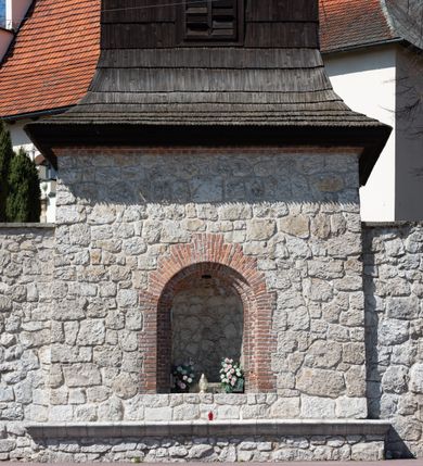 Zdjęcie nr 99: Kościół orientowany, murowany, jednonawowy z węższym prezbiterium zakończonym półkolistą absydą. Przy prezbiterium od północy znajduje się zakrystia, od południa kwadratowa kaplica św. Anny, a przy nawie od południa kruchta. Wnętrze kościoła nakryte jest nowym stropem, natomiast w kaplicy znajduje się sklepienie krzyżowo-żebrowe. Fasada zachodnia ujęta jest na narożnikach skośnymi szkarpami i zwieńczona schodkowym szczytem, podobnie zwieńczona jest kruchta południowa. Portal zachodni kamienny, z belkowaniem wspartym na dwóch liściastych konsolach ponad którymi edikula z płaskorzeźbionym krucyfiksem i klęczącymi postaciami męskimi. Na belkowaniu znajdują się dwa kartusze z herbami: po lewej herb Bończa, a nad nim litery „I” oraz „T”, a na prawo herb Szreniawa i litery „B” i „T”. Portal kruchty południowej jest również kamienny, podobny do zachodniego z inskrypcją: „IN LAVDEM ET GL[ORI]AM DEI O[MN]IP[OTENTIS] HO[NO]RE[M] / B(EATE) M(ARIAE) S(ANCTAE) V(IRGINIS) S(ANCTUS) AEGIDY ET OM(NIUM) SS. FIR. REGNÃTE [TERTIO] SIGISM[UN]DO / REGE POL[ONIAE] Z[?] HEMO[?] EP[ISCOP]O CRAC(OVIENSIS) BERN[AR]DO MACIEIOWSKI / NOVIT[ER] CAR[DINA]LI CRA[COVIENSE] DEI FACTO INTERI[M] PLEBA[N]O R[E]V[EREN]DO SEB(ASTIANO) / NAGRODIO A I SYRADIA PHI[LOSOPHI]AE DOCTORE COLLEG[I]A [MA]IORE / S. T(HEOLOGIAE) PVBLICO PROFES(SORE) PRAEP[OSI]TO S(ANCTA) AN(NAE) CRAC[OVIAE] DECIMARVM / ET FVNDI ECCL(ESIA)E HVIVS P[OST] IVRIS STREPITV(M) RESTITV / TORE ANNO OCTAVO PLEBANAT[U]S SVI. TEMPLVM HO(C) / [ dwa wiersze skute] DE' / NOWO AEDIFICATVM. ET. CONSTRVCTVM. ADIVTORIO / QVORVNDÃ ANNO D[OMINI] MDCIIII MENSE SEPTEMB[RE]”. Od południa świątyni umieszczone są trzy otwory okienne w kształcie stojących prostokątów, zamkniętych łukiem półkolistym, a w prezbiterium dwa małe okrągłe okna. Kościół nakryty jest dwoma dwuspadowymi dachami, nad prezbiterium nieco niższym, nad nawą zwieńczonym wąską i wysoką sygnaturką na dzwon. Wewnątrz świątyni na skrzyżowaniu nawy i prezbiterium umocowana jest drewniana belka tęczowa z ustawionym na niej krucyfiksem i figurami Matki Boskiej i św. Jana Ewangelisty. Chór zachodni drewniany, na planie prostokąta, pośrodku półkoliście zamknięty, wsparty na sześciu filarach, od północnego zachodu z obudowaną boazerią klatką schodową. 