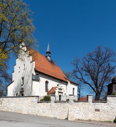 Zdjęcie nr 19: Kościół orientowany, murowany, jednonawowy z węższym prezbiterium zakończonym półkolistą absydą. Przy prezbiterium od północy znajduje się zakrystia, od południa kwadratowa kaplica św. Anny, a przy nawie od południa kruchta. Wnętrze kościoła nakryte jest nowym stropem, natomiast w kaplicy znajduje się sklepienie krzyżowo-żebrowe. Fasada zachodnia ujęta jest na narożnikach skośnymi szkarpami i zwieńczona schodkowym szczytem, podobnie zwieńczona jest kruchta południowa. Portal zachodni kamienny, z belkowaniem wspartym na dwóch liściastych konsolach ponad którymi edikula z płaskorzeźbionym krucyfiksem i klęczącymi postaciami męskimi. Na belkowaniu znajdują się dwa kartusze z herbami: po lewej herb Bończa, a nad nim litery „I” oraz „T”, a na prawo herb Szreniawa i litery „B” i „T”. Portal kruchty południowej jest również kamienny, podobny do zachodniego z inskrypcją: „IN LAVDEM ET GL[ORI]AM DEI O[MN]IP[OTENTIS] HO[NO]RE[M] / B(EATE) M(ARIAE) S(ANCTAE) V(IRGINIS) S(ANCTUS) AEGIDY ET OM(NIUM) SS. FIR. REGNÃTE [TERTIO] SIGISM[UN]DO / REGE POL[ONIAE] Z[?] HEMO[?] EP[ISCOP]O CRAC(OVIENSIS) BERN[AR]DO MACIEIOWSKI / NOVIT[ER] CAR[DINA]LI CRA[COVIENSE] DEI FACTO INTERI[M] PLEBA[N]O R[E]V[EREN]DO SEB(ASTIANO) / NAGRODIO A I SYRADIA PHI[LOSOPHI]AE DOCTORE COLLEG[I]A [MA]IORE / S. T(HEOLOGIAE) PVBLICO PROFES(SORE) PRAEP[OSI]TO S(ANCTA) AN(NAE) CRAC[OVIAE] DECIMARVM / ET FVNDI ECCL(ESIA)E HVIVS P[OST] IVRIS STREPITV(M) RESTITV / TORE ANNO OCTAVO PLEBANAT[U]S SVI. TEMPLVM HO(C) / [ dwa wiersze skute] DE' / NOWO AEDIFICATVM. ET. CONSTRVCTVM. ADIVTORIO / QVORVNDÃ ANNO D[OMINI] MDCIIII MENSE SEPTEMB[RE]”. Od południa świątyni umieszczone są trzy otwory okienne w kształcie stojących prostokątów, zamkniętych łukiem półkolistym, a w prezbiterium dwa małe okrągłe okna. Kościół nakryty jest dwoma dwuspadowymi dachami, nad prezbiterium nieco niższym, nad nawą zwieńczonym wąską i wysoką sygnaturką na dzwon. Wewnątrz świątyni na skrzyżowaniu nawy i prezbiterium umocowana jest drewniana belka tęczowa z ustawionym na niej krucyfiksem i figurami Matki Boskiej i św. Jana Ewangelisty. Chór zachodni drewniany, na planie prostokąta, pośrodku półkoliście zamknięty, wsparty na sześciu filarach, od północnego zachodu z obudowaną boazerią klatką schodową. 