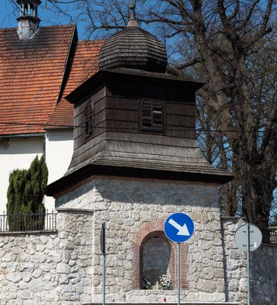 Zdjęcie nr 100: Kościół orientowany, murowany, jednonawowy z węższym prezbiterium zakończonym półkolistą absydą. Przy prezbiterium od północy znajduje się zakrystia, od południa kwadratowa kaplica św. Anny, a przy nawie od południa kruchta. Wnętrze kościoła nakryte jest nowym stropem, natomiast w kaplicy znajduje się sklepienie krzyżowo-żebrowe. Fasada zachodnia ujęta jest na narożnikach skośnymi szkarpami i zwieńczona schodkowym szczytem, podobnie zwieńczona jest kruchta południowa. Portal zachodni kamienny, z belkowaniem wspartym na dwóch liściastych konsolach ponad którymi edikula z płaskorzeźbionym krucyfiksem i klęczącymi postaciami męskimi. Na belkowaniu znajdują się dwa kartusze z herbami: po lewej herb Bończa, a nad nim litery „I” oraz „T”, a na prawo herb Szreniawa i litery „B” i „T”. Portal kruchty południowej jest również kamienny, podobny do zachodniego z inskrypcją: „IN LAVDEM ET GL[ORI]AM DEI O[MN]IP[OTENTIS] HO[NO]RE[M] / B(EATE) M(ARIAE) S(ANCTAE) V(IRGINIS) S(ANCTUS) AEGIDY ET OM(NIUM) SS. FIR. REGNÃTE [TERTIO] SIGISM[UN]DO / REGE POL[ONIAE] Z[?] HEMO[?] EP[ISCOP]O CRAC(OVIENSIS) BERN[AR]DO MACIEIOWSKI / NOVIT[ER] CAR[DINA]LI CRA[COVIENSE] DEI FACTO INTERI[M] PLEBA[N]O R[E]V[EREN]DO SEB(ASTIANO) / NAGRODIO A I SYRADIA PHI[LOSOPHI]AE DOCTORE COLLEG[I]A [MA]IORE / S. T(HEOLOGIAE) PVBLICO PROFES(SORE) PRAEP[OSI]TO S(ANCTA) AN(NAE) CRAC[OVIAE] DECIMARVM / ET FVNDI ECCL(ESIA)E HVIVS P[OST] IVRIS STREPITV(M) RESTITV / TORE ANNO OCTAVO PLEBANAT[U]S SVI. TEMPLVM HO(C) / [ dwa wiersze skute] DE' / NOWO AEDIFICATVM. ET. CONSTRVCTVM. ADIVTORIO / QVORVNDÃ ANNO D[OMINI] MDCIIII MENSE SEPTEMB[RE]”. Od południa świątyni umieszczone są trzy otwory okienne w kształcie stojących prostokątów, zamkniętych łukiem półkolistym, a w prezbiterium dwa małe okrągłe okna. Kościół nakryty jest dwoma dwuspadowymi dachami, nad prezbiterium nieco niższym, nad nawą zwieńczonym wąską i wysoką sygnaturką na dzwon. Wewnątrz świątyni na skrzyżowaniu nawy i prezbiterium umocowana jest drewniana belka tęczowa z ustawionym na niej krucyfiksem i figurami Matki Boskiej i św. Jana Ewangelisty. Chór zachodni drewniany, na planie prostokąta, pośrodku półkoliście zamknięty, wsparty na sześciu filarach, od północnego zachodu z obudowaną boazerią klatką schodową. 