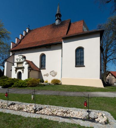Zdjęcie nr 41: Kościół orientowany, murowany, jednonawowy z węższym prezbiterium zakończonym półkolistą absydą. Przy prezbiterium od północy znajduje się zakrystia, od południa kwadratowa kaplica św. Anny, a przy nawie od południa kruchta. Wnętrze kościoła nakryte jest nowym stropem, natomiast w kaplicy znajduje się sklepienie krzyżowo-żebrowe. Fasada zachodnia ujęta jest na narożnikach skośnymi szkarpami i zwieńczona schodkowym szczytem, podobnie zwieńczona jest kruchta południowa. Portal zachodni kamienny, z belkowaniem wspartym na dwóch liściastych konsolach ponad którymi edikula z płaskorzeźbionym krucyfiksem i klęczącymi postaciami męskimi. Na belkowaniu znajdują się dwa kartusze z herbami: po lewej herb Bończa, a nad nim litery „I” oraz „T”, a na prawo herb Szreniawa i litery „B” i „T”. Portal kruchty południowej jest również kamienny, podobny do zachodniego z inskrypcją: „IN LAVDEM ET GL[ORI]AM DEI O[MN]IP[OTENTIS] HO[NO]RE[M] / B(EATE) M(ARIAE) S(ANCTAE) V(IRGINIS) S(ANCTUS) AEGIDY ET OM(NIUM) SS. FIR. REGNÃTE [TERTIO] SIGISM[UN]DO / REGE POL[ONIAE] Z[?] HEMO[?] EP[ISCOP]O CRAC(OVIENSIS) BERN[AR]DO MACIEIOWSKI / NOVIT[ER] CAR[DINA]LI CRA[COVIENSE] DEI FACTO INTERI[M] PLEBA[N]O R[E]V[EREN]DO SEB(ASTIANO) / NAGRODIO A I SYRADIA PHI[LOSOPHI]AE DOCTORE COLLEG[I]A [MA]IORE / S. T(HEOLOGIAE) PVBLICO PROFES(SORE) PRAEP[OSI]TO S(ANCTA) AN(NAE) CRAC[OVIAE] DECIMARVM / ET FVNDI ECCL(ESIA)E HVIVS P[OST] IVRIS STREPITV(M) RESTITV / TORE ANNO OCTAVO PLEBANAT[U]S SVI. TEMPLVM HO(C) / [ dwa wiersze skute] DE' / NOWO AEDIFICATVM. ET. CONSTRVCTVM. ADIVTORIO / QVORVNDÃ ANNO D[OMINI] MDCIIII MENSE SEPTEMB[RE]”. Od południa świątyni umieszczone są trzy otwory okienne w kształcie stojących prostokątów, zamkniętych łukiem półkolistym, a w prezbiterium dwa małe okrągłe okna. Kościół nakryty jest dwoma dwuspadowymi dachami, nad prezbiterium nieco niższym, nad nawą zwieńczonym wąską i wysoką sygnaturką na dzwon. Wewnątrz świątyni na skrzyżowaniu nawy i prezbiterium umocowana jest drewniana belka tęczowa z ustawionym na niej krucyfiksem i figurami Matki Boskiej i św. Jana Ewangelisty. Chór zachodni drewniany, na planie prostokąta, pośrodku półkoliście zamknięty, wsparty na sześciu filarach, od północnego zachodu z obudowaną boazerią klatką schodową. 