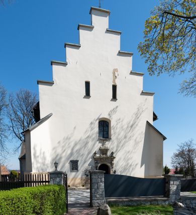 Zdjęcie nr 11: Kościół orientowany, murowany, jednonawowy z węższym prezbiterium zakończonym półkolistą absydą. Przy prezbiterium od północy znajduje się zakrystia, od południa kwadratowa kaplica św. Anny, a przy nawie od południa kruchta. Wnętrze kościoła nakryte jest nowym stropem, natomiast w kaplicy znajduje się sklepienie krzyżowo-żebrowe. Fasada zachodnia ujęta jest na narożnikach skośnymi szkarpami i zwieńczona schodkowym szczytem, podobnie zwieńczona jest kruchta południowa. Portal zachodni kamienny, z belkowaniem wspartym na dwóch liściastych konsolach ponad którymi edikula z płaskorzeźbionym krucyfiksem i klęczącymi postaciami męskimi. Na belkowaniu znajdują się dwa kartusze z herbami: po lewej herb Bończa, a nad nim litery „I” oraz „T”, a na prawo herb Szreniawa i litery „B” i „T”. Portal kruchty południowej jest również kamienny, podobny do zachodniego z inskrypcją: „IN LAVDEM ET GL[ORI]AM DEI O[MN]IP[OTENTIS] HO[NO]RE[M] / B(EATE) M(ARIAE) S(ANCTAE) V(IRGINIS) S(ANCTUS) AEGIDY ET OM(NIUM) SS. FIR. REGNÃTE [TERTIO] SIGISM[UN]DO / REGE POL[ONIAE] Z[?] HEMO[?] EP[ISCOP]O CRAC(OVIENSIS) BERN[AR]DO MACIEIOWSKI / NOVIT[ER] CAR[DINA]LI CRA[COVIENSE] DEI FACTO INTERI[M] PLEBA[N]O R[E]V[EREN]DO SEB(ASTIANO) / NAGRODIO A I SYRADIA PHI[LOSOPHI]AE DOCTORE COLLEG[I]A [MA]IORE / S. T(HEOLOGIAE) PVBLICO PROFES(SORE) PRAEP[OSI]TO S(ANCTA) AN(NAE) CRAC[OVIAE] DECIMARVM / ET FVNDI ECCL(ESIA)E HVIVS P[OST] IVRIS STREPITV(M) RESTITV / TORE ANNO OCTAVO PLEBANAT[U]S SVI. TEMPLVM HO(C) / [ dwa wiersze skute] DE' / NOWO AEDIFICATVM. ET. CONSTRVCTVM. ADIVTORIO / QVORVNDÃ ANNO D[OMINI] MDCIIII MENSE SEPTEMB[RE]”. Od południa świątyni umieszczone są trzy otwory okienne w kształcie stojących prostokątów, zamkniętych łukiem półkolistym, a w prezbiterium dwa małe okrągłe okna. Kościół nakryty jest dwoma dwuspadowymi dachami, nad prezbiterium nieco niższym, nad nawą zwieńczonym wąską i wysoką sygnaturką na dzwon. Wewnątrz świątyni na skrzyżowaniu nawy i prezbiterium umocowana jest drewniana belka tęczowa z ustawionym na niej krucyfiksem i figurami Matki Boskiej i św. Jana Ewangelisty. Chór zachodni drewniany, na planie prostokąta, pośrodku półkoliście zamknięty, wsparty na sześciu filarach, od północnego zachodu z obudowaną boazerią klatką schodową. 